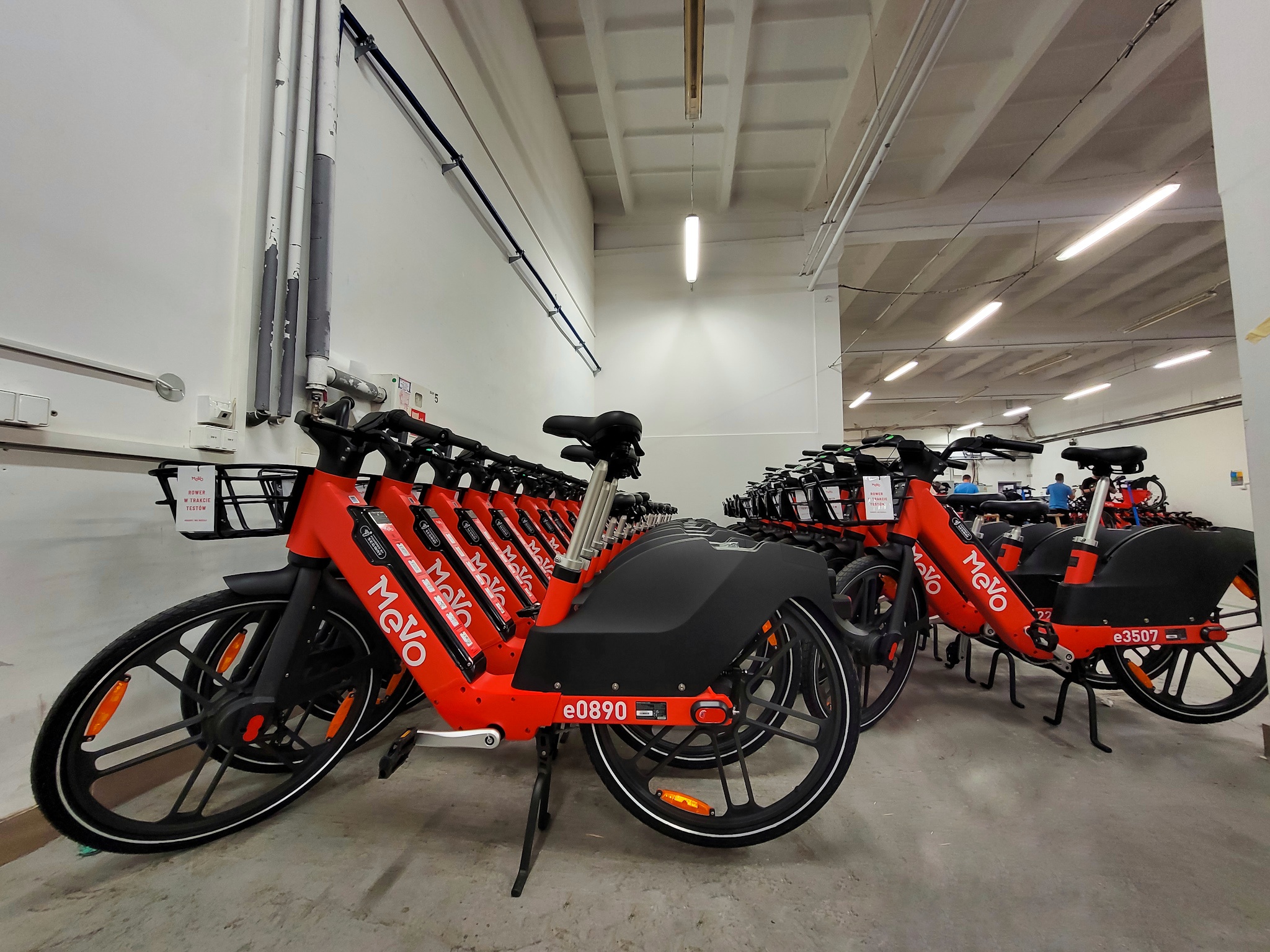 Kilkadziesiąt czerwonych rowerów mevo, ustawione w równym szeregu, w środku hali magazynowej