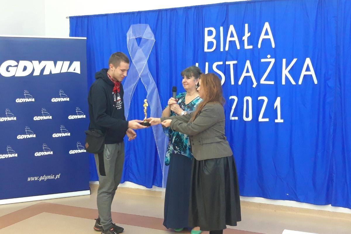 Mężczyzna odbiera statuetkę od 2 kobiet