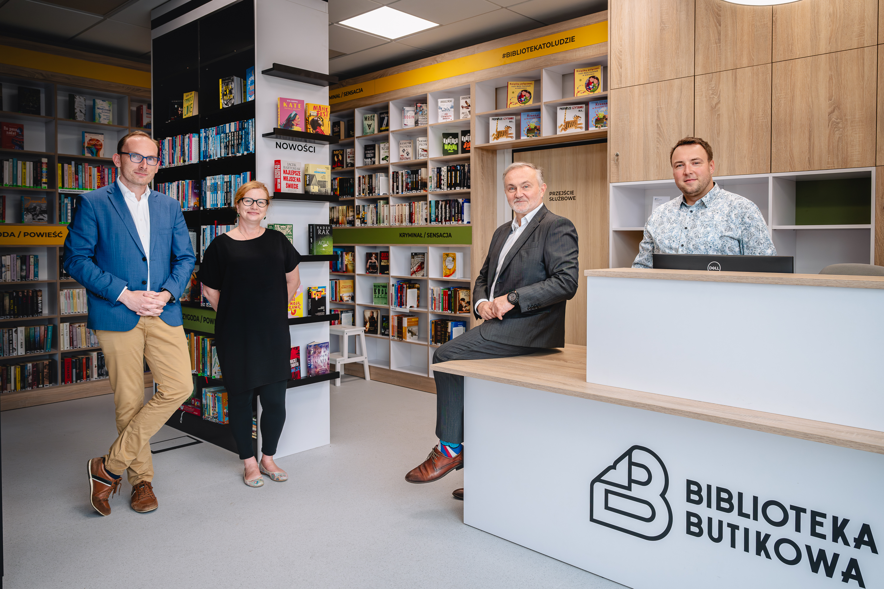 Jakub Ubych, Natalia Gromow, Wojciech Szczurek i Sebastian Gańczak pozują do zdjęcia w Bibliotece Butikowej, za nimi regały z książkami