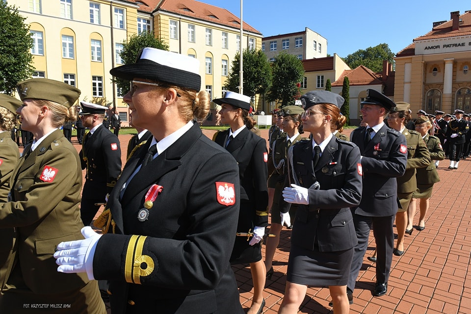 Akademia Marynarki Wojennej, plac, w tle budynek, uroczystość promocji oficerskiej, maszerują w szeregach kobiety i mężczyźni oficerowie, w tle żołnierze