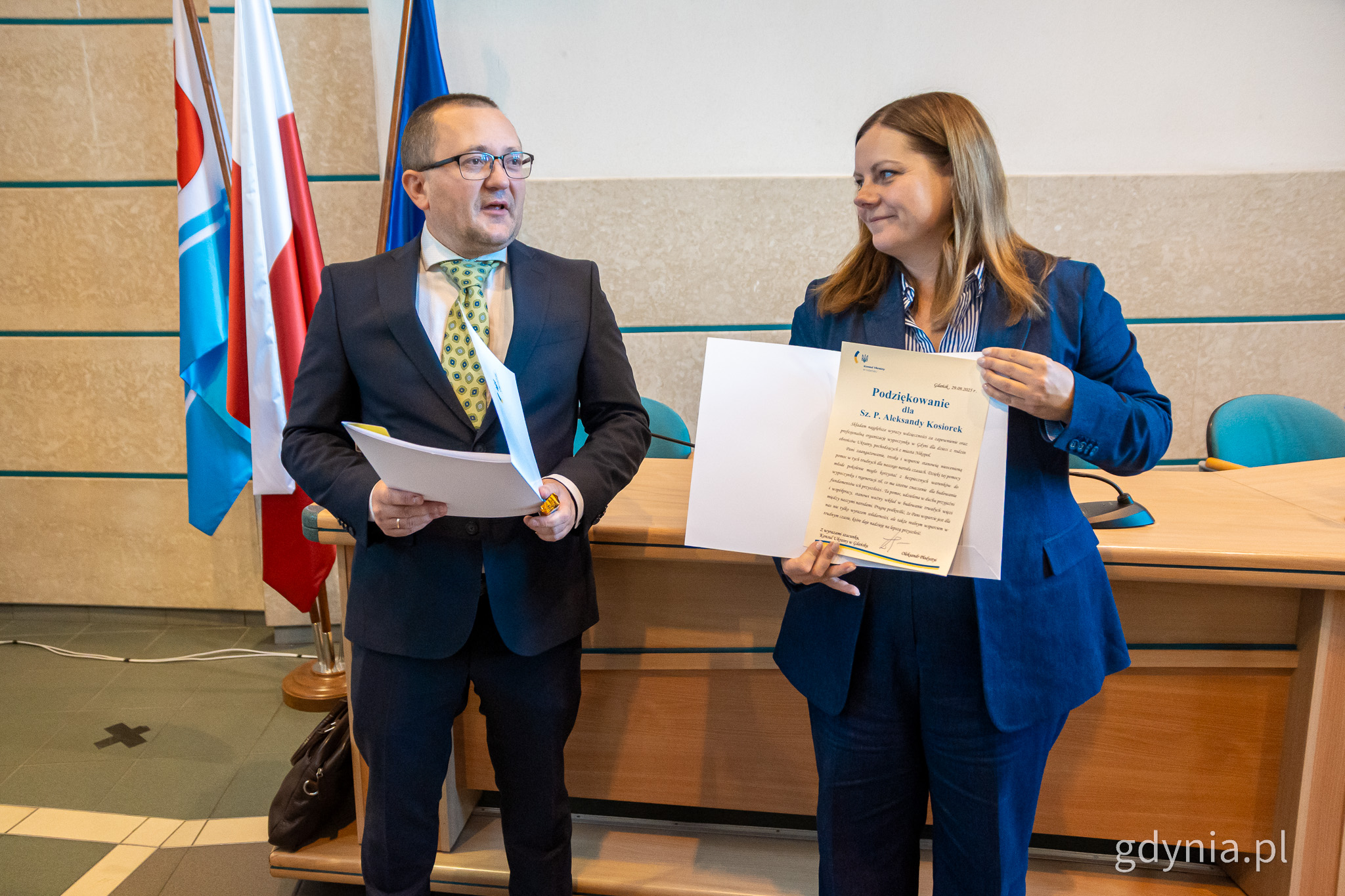 Sala 105 w Urzedzie Miasta Gdyni, stoją Oleksandr Płodystyi i prezydent Aleksandra Kosiorek, prezydent prezentuje treść listu z podziękowaniami