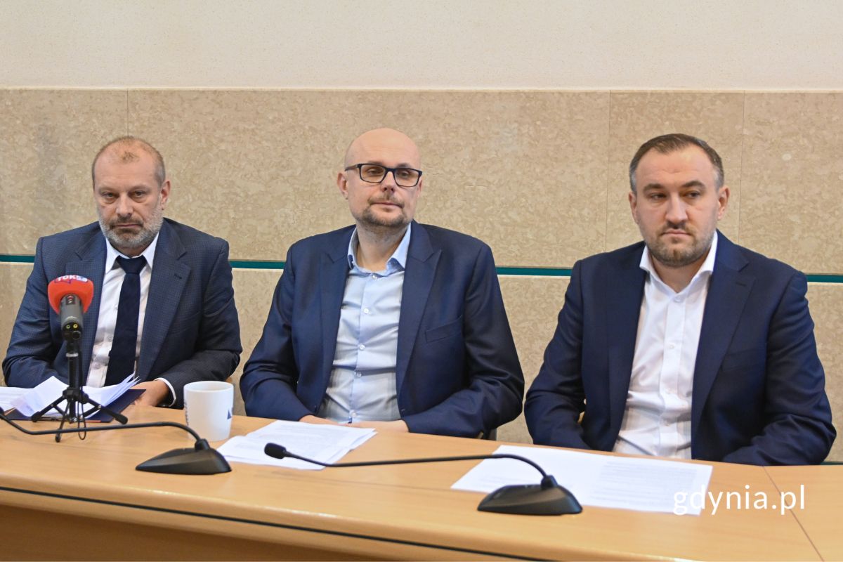 Trzej mężczyźni siedzący przy stole, na którym stoją mikrofony