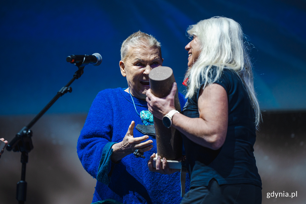 Starsza kobieta odbiera nagrodę podr&oacute;żniczą od innej kobiety.