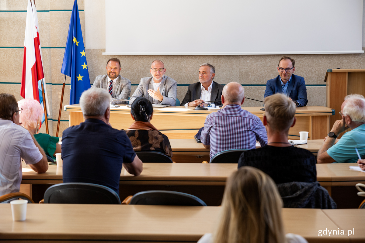 Czworo gdyńskich samorządowc&oacute;w siedzi za pulpitem przed przedstawicielami działkowc&oacute;w. 