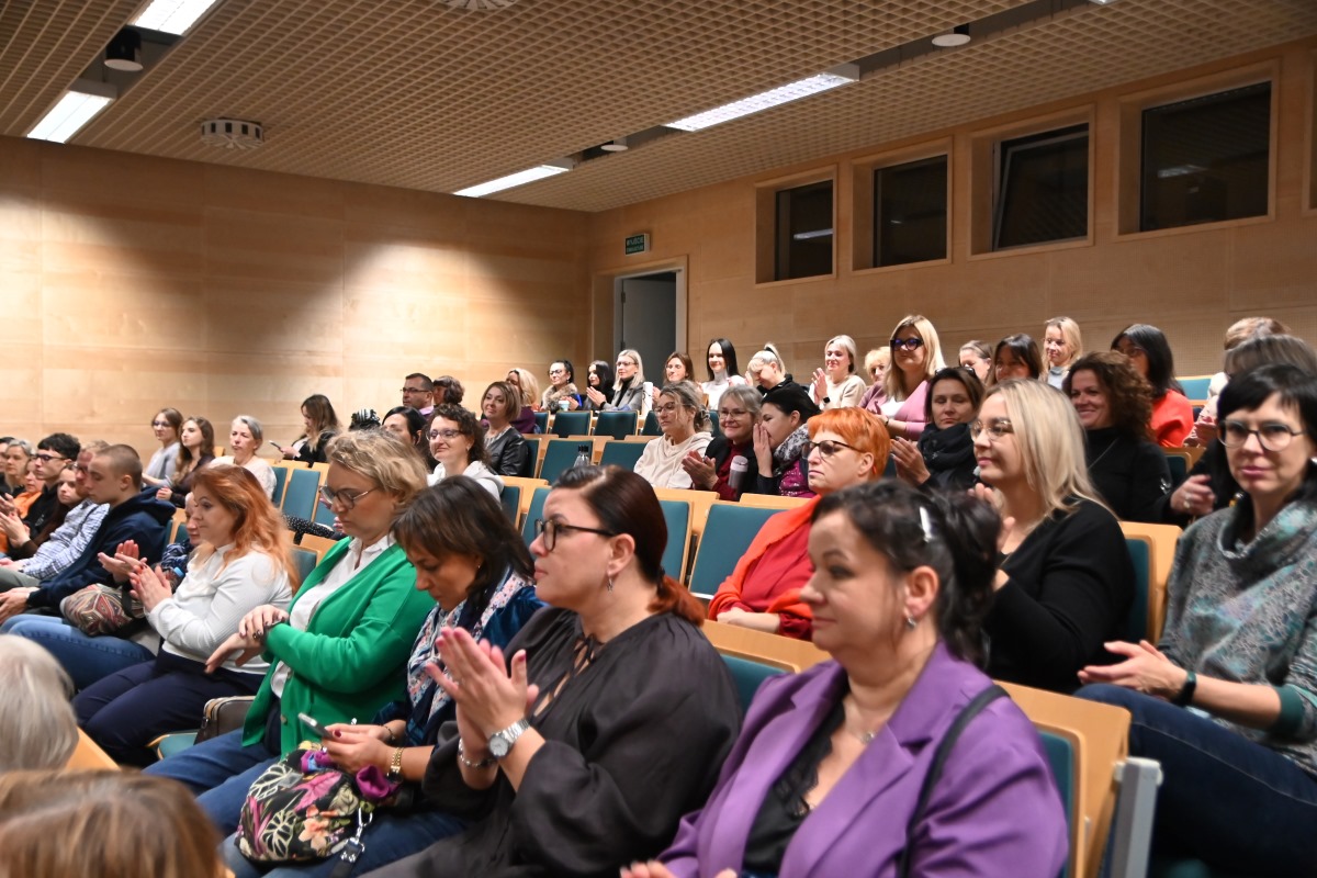 Duża grupa ludzi - słuchaczy w r&oacute;żnym wieku, w auli. 