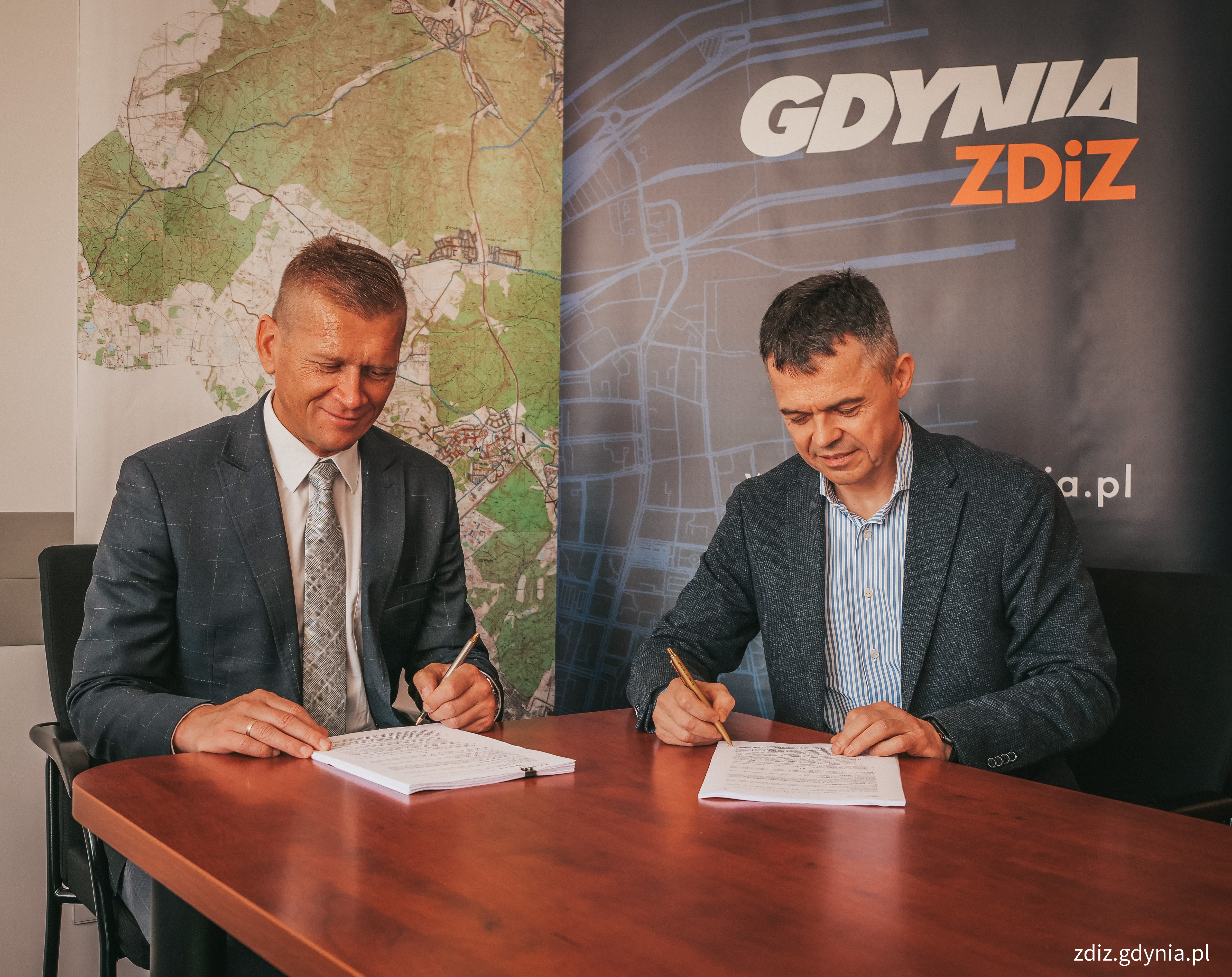dwie osoby podpisujące umowę, w tle logo Gdynia ZDiZ