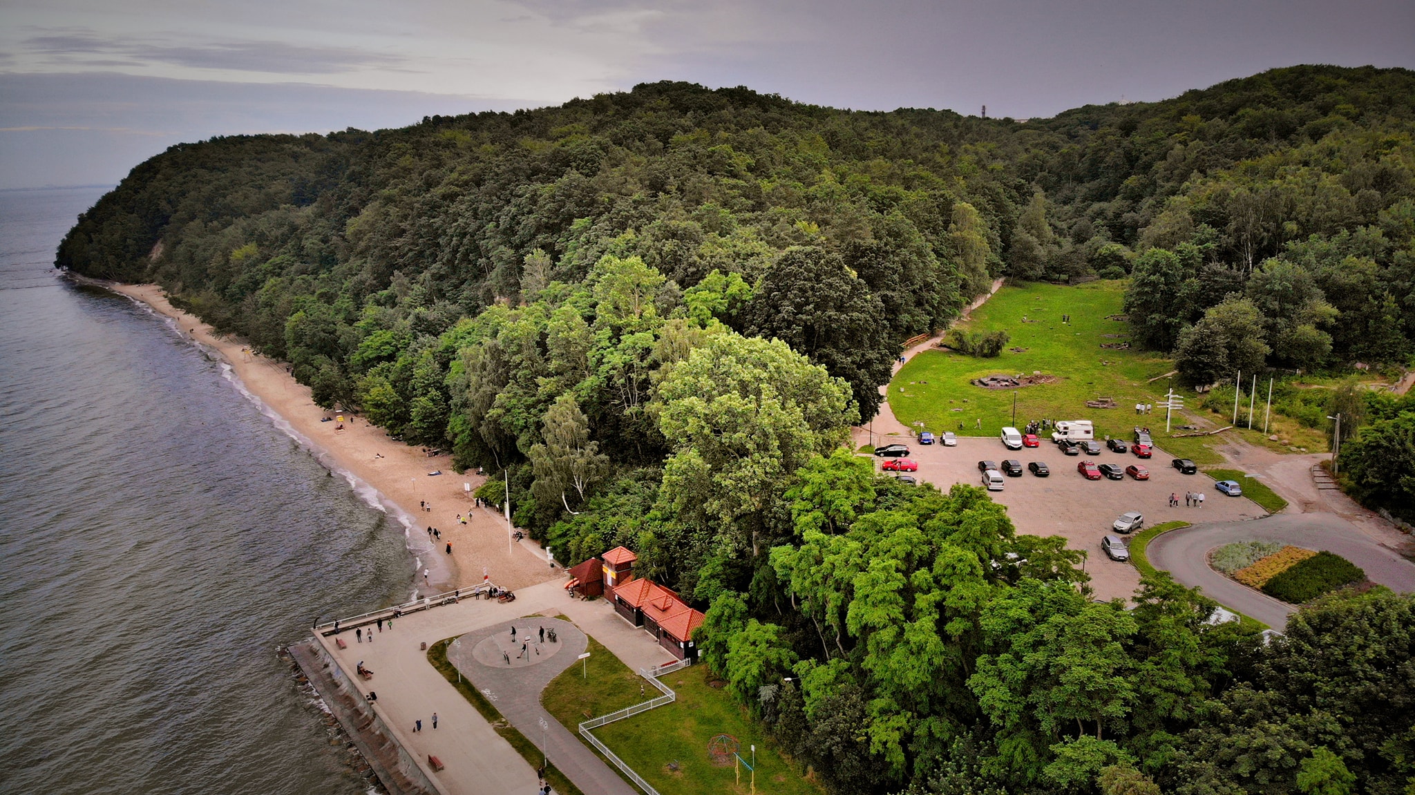 Widok z lotu ptaka na nadmorską polanę otoczoną lasem i wzg&oacute;rzami.