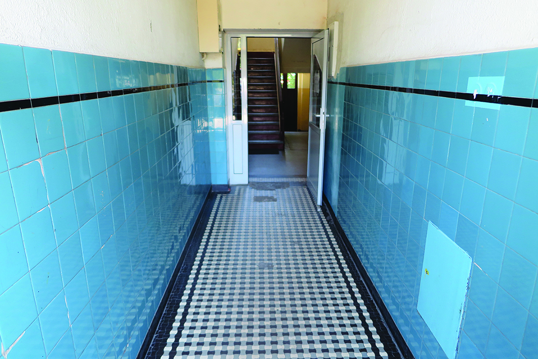 Strefa wejściowa w kamienicy przy ul. Portowej 3, dolne partie ścian wykończone ceramicznymi błękitnymi płytkami z wykończeniem z czarnym paskiem, posadzka zakomponowana z czarno-białych płytek tzw. gorsecik&oacute;w.