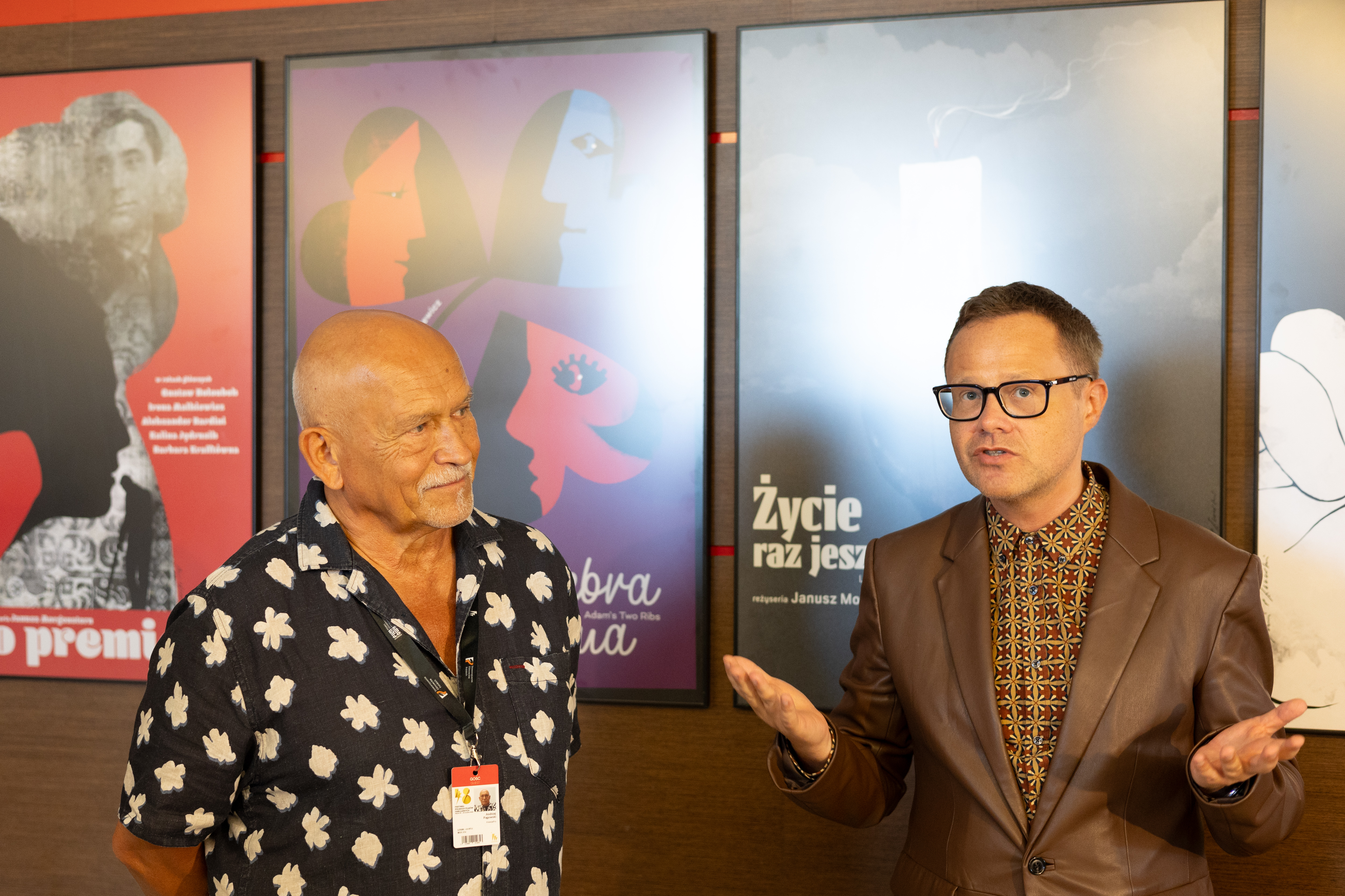 Foyer Teatru Muzycznego, dw&oacute;ch mężczyzn na środku, za nimi plakaty filmowe