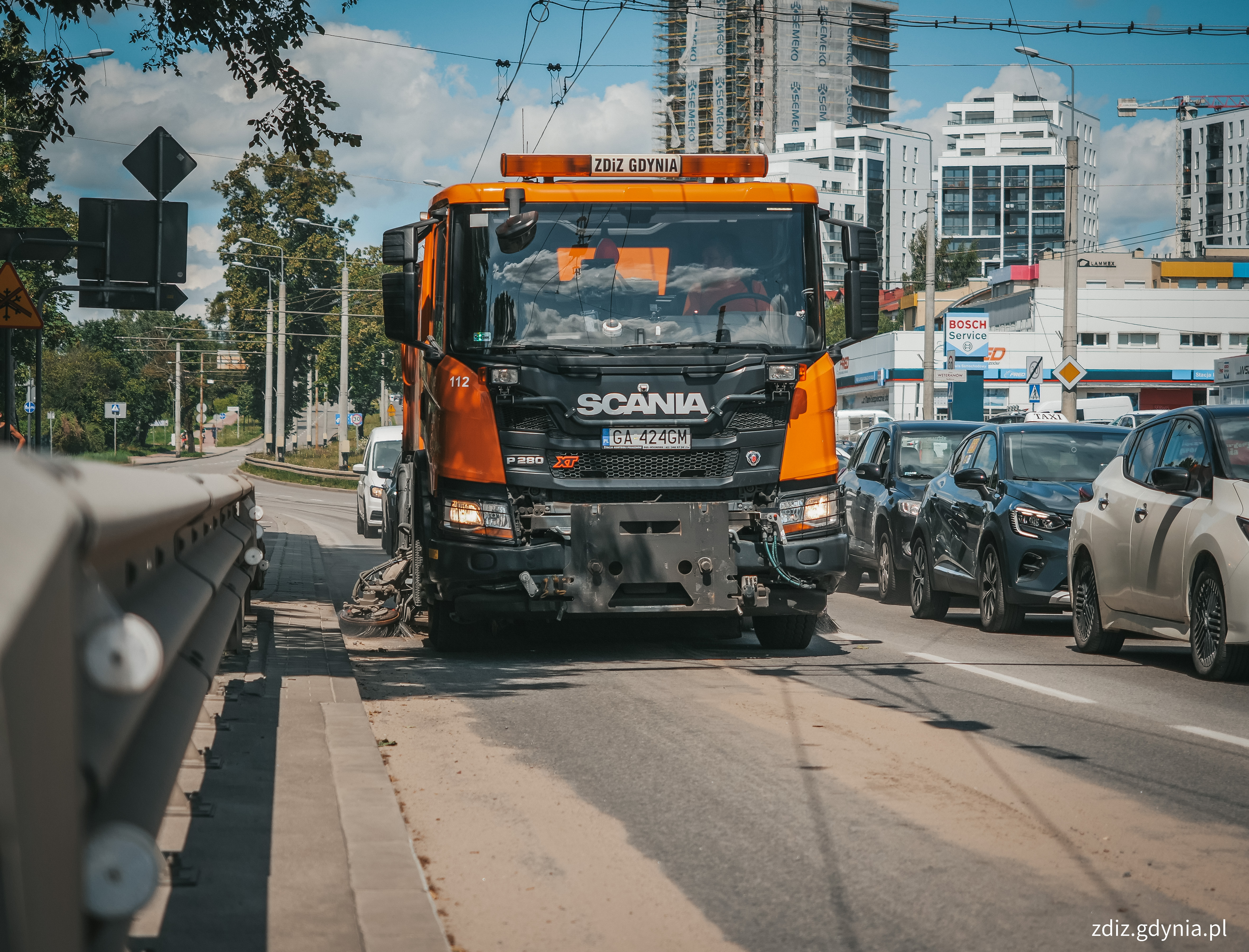 pojazd do oczyszczania ulic w ruchu ulicznym, w tle inne pojazdy i budynki