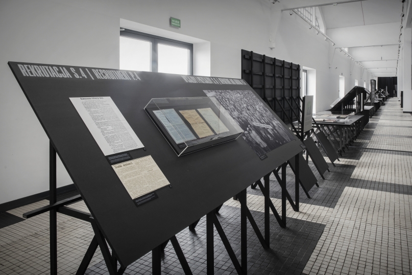 Zdjęcie eksponat&oacute;w z wystawy "Carboland" w Muzeum Emigracji. Na zdjęciu widać czarną ściankę z przyklejonymi opisami i szklaną gablotką z eksponatami. Na g&oacute;rze widnieje napis "Rekrutacja S.4". // fot. Muzeum Emigracji