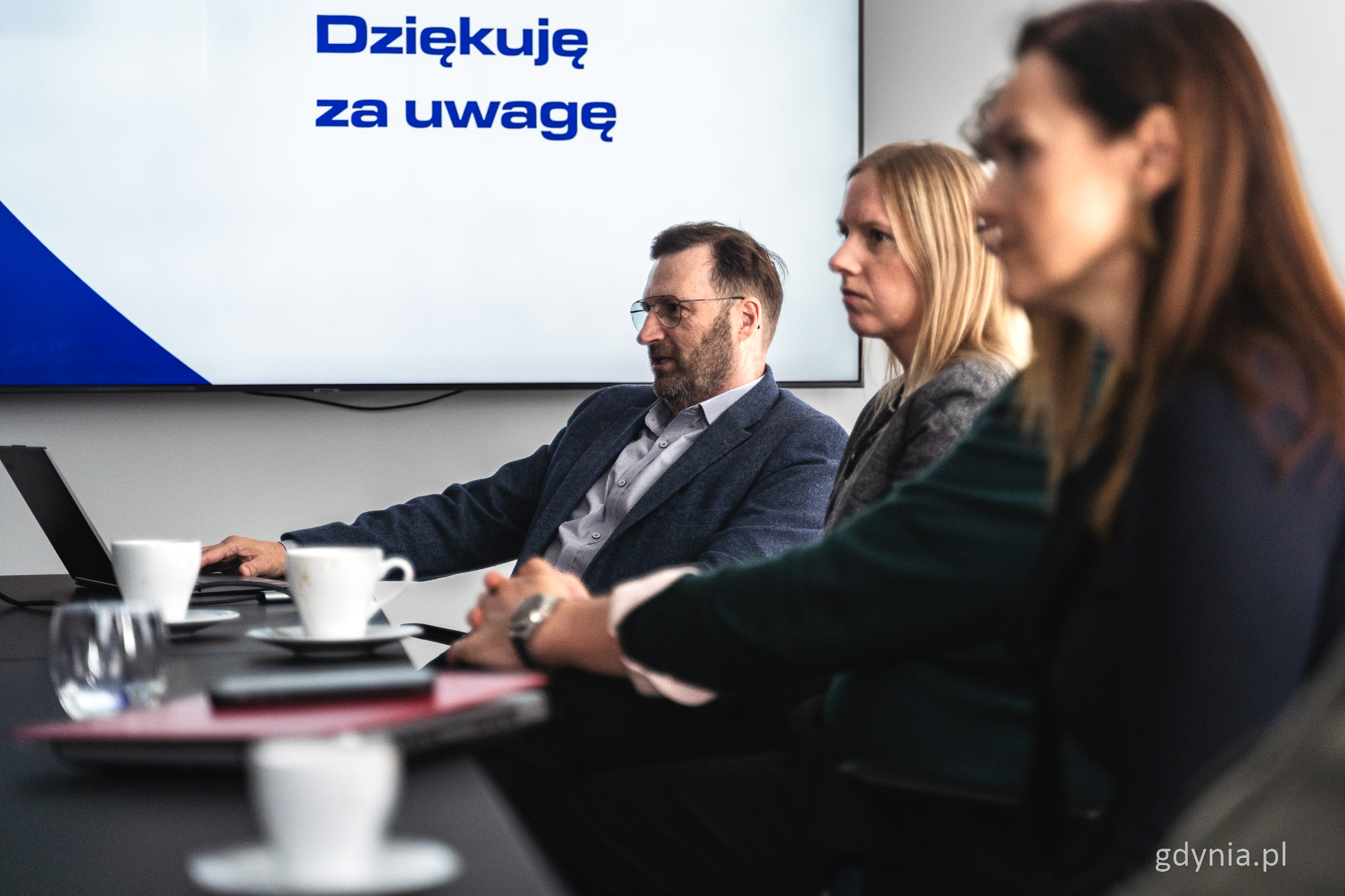 Sala konferencyjna, st&oacute;ł, kilka os&oacute;b siedzi przy stole, widoczny ekran