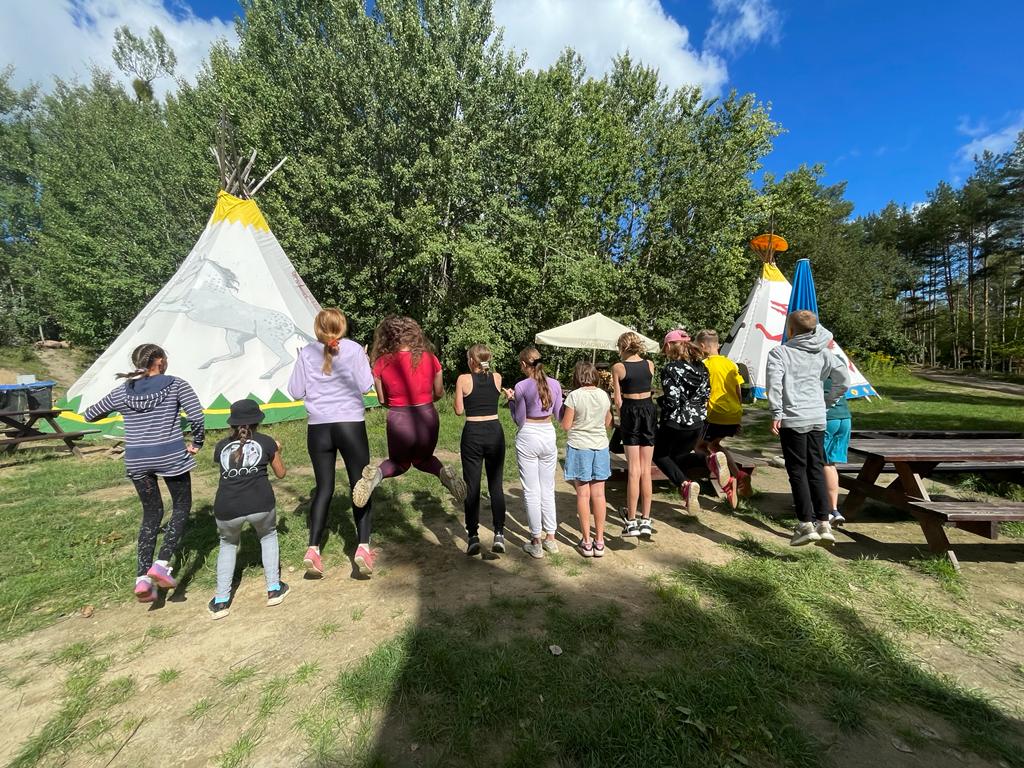 Grupa ustawionych w szeregu dzieci przed tipi