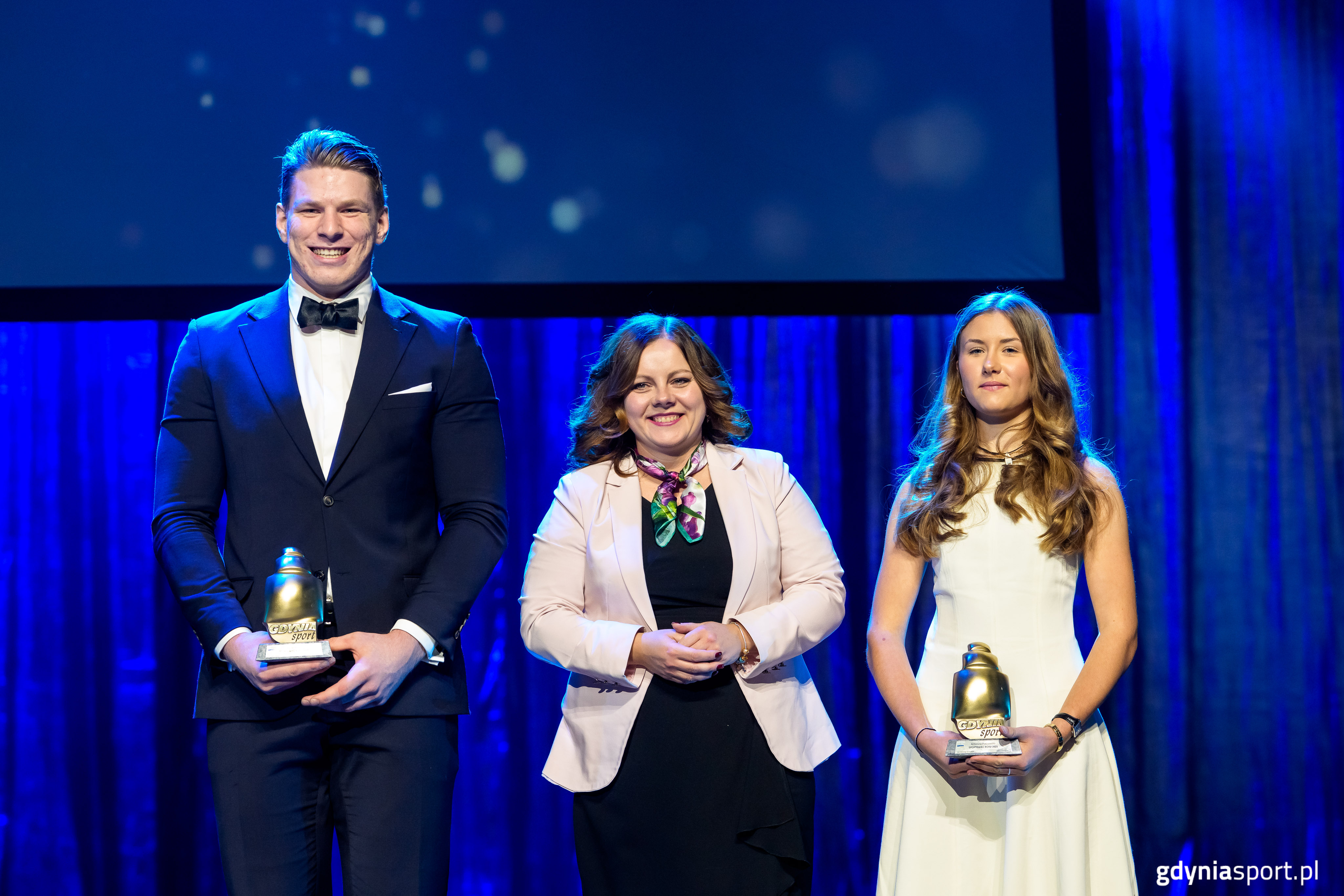 Scena w Teatrze Muzycznym, niebieskie tło, stoją Jakub Sordyl, Aleksandra Kosiorek i Antonina Puchowska
