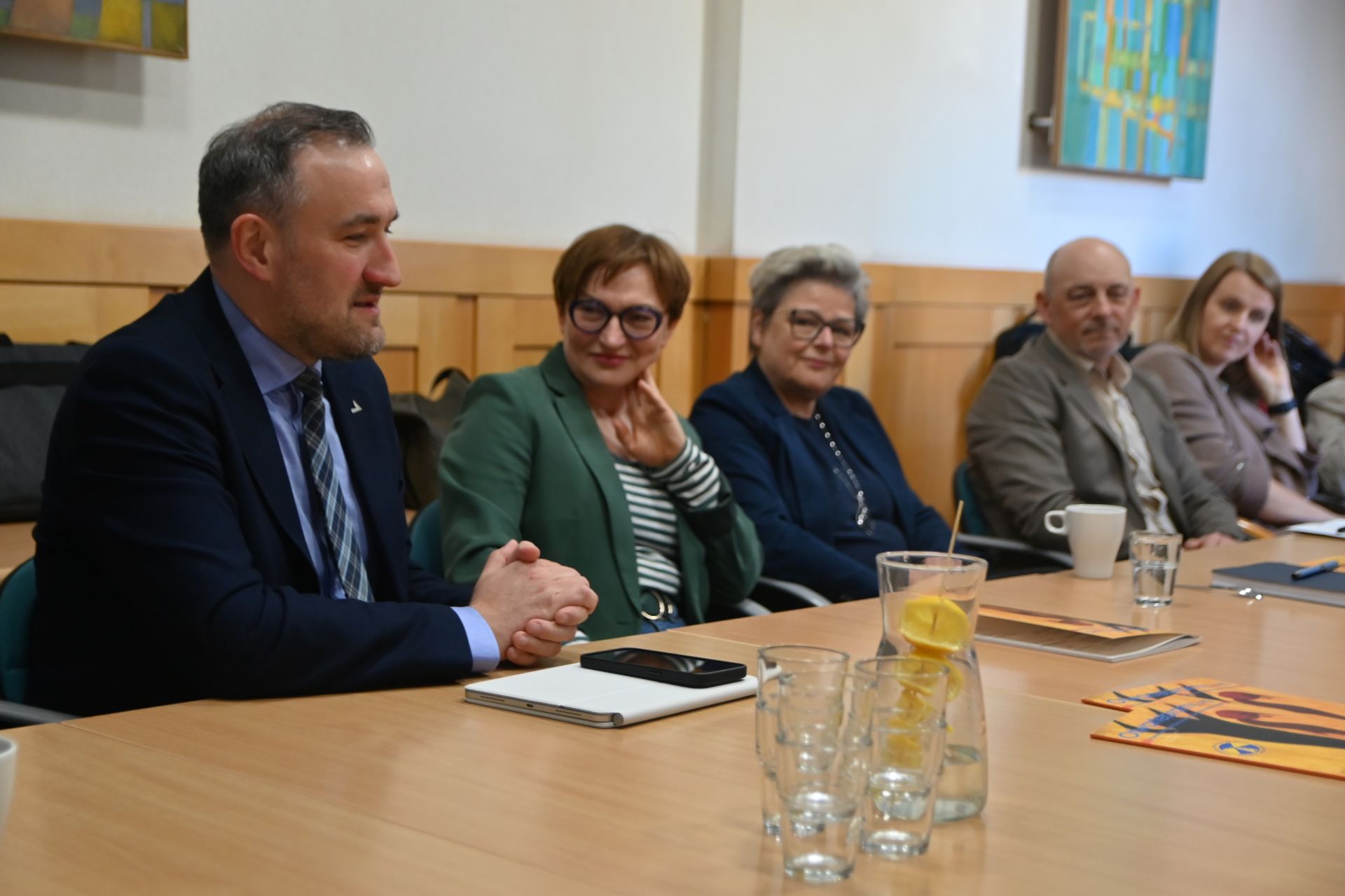 Grupa ludzi w r&oacute;żnym wieku dyskutujących przy stole 