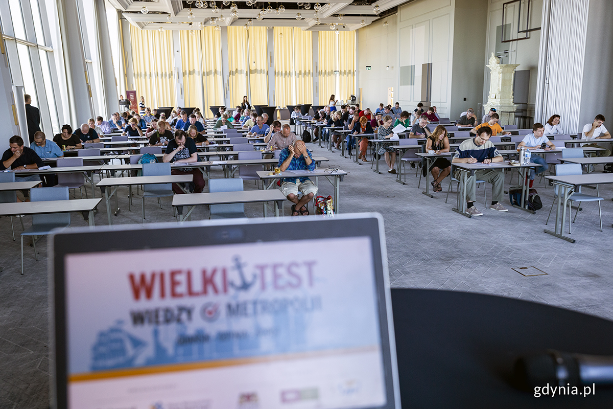 Ludzie siedzą na sali i rozwiązują test.