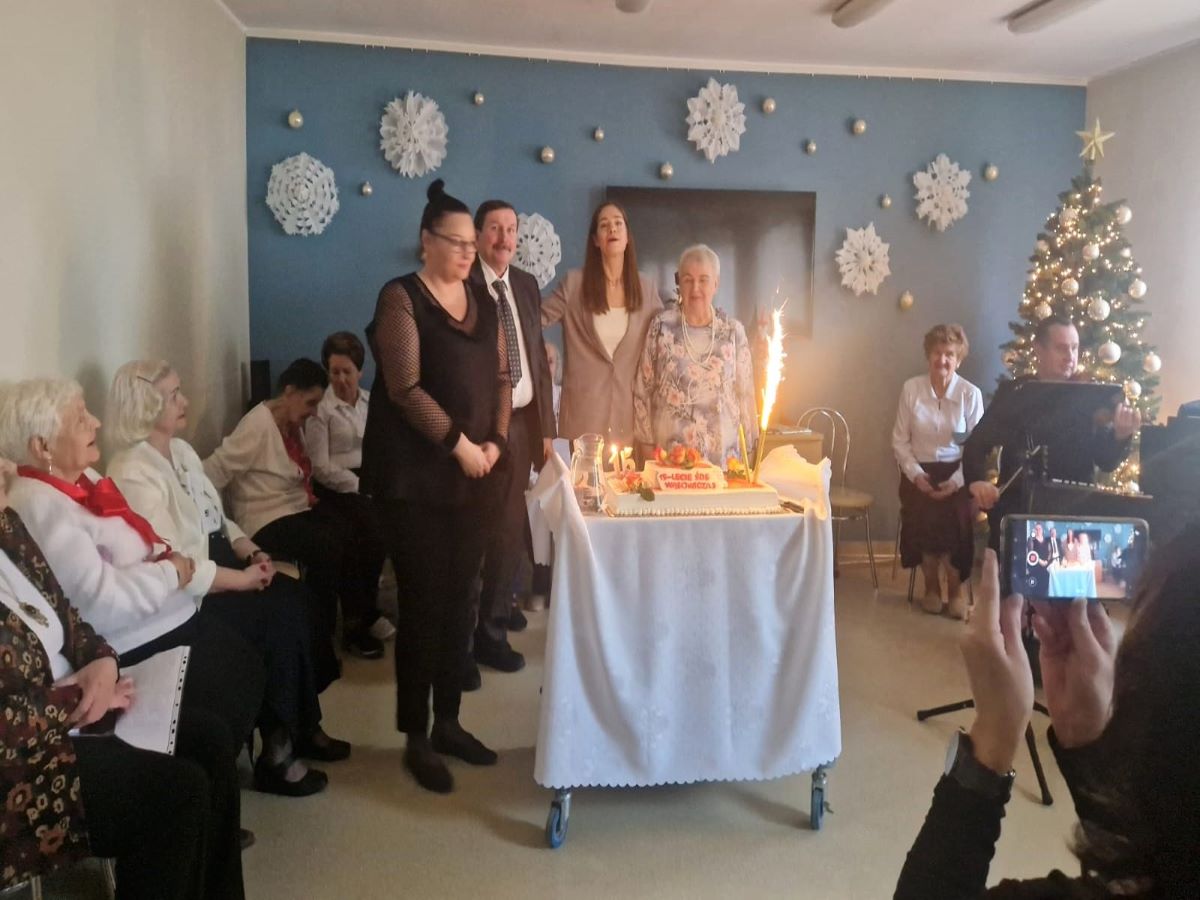 Zdjęcie przedstawia uczestnik&oacute;w zajęć i kadrę Środowiskowego Domu Samopomocy przy Wąsowicza 3 stojących przy torcie urodzinowym z okazji jubileuszu 15-lecia działania plac&oacute;wki.