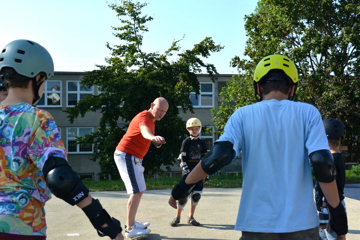 Zdjęcie przedstawia p. Waldemara Zadorożnego pokazującego dzieciom spos&oacute;b wykonania ćwiczenia podczas treningu z deskorolką. 