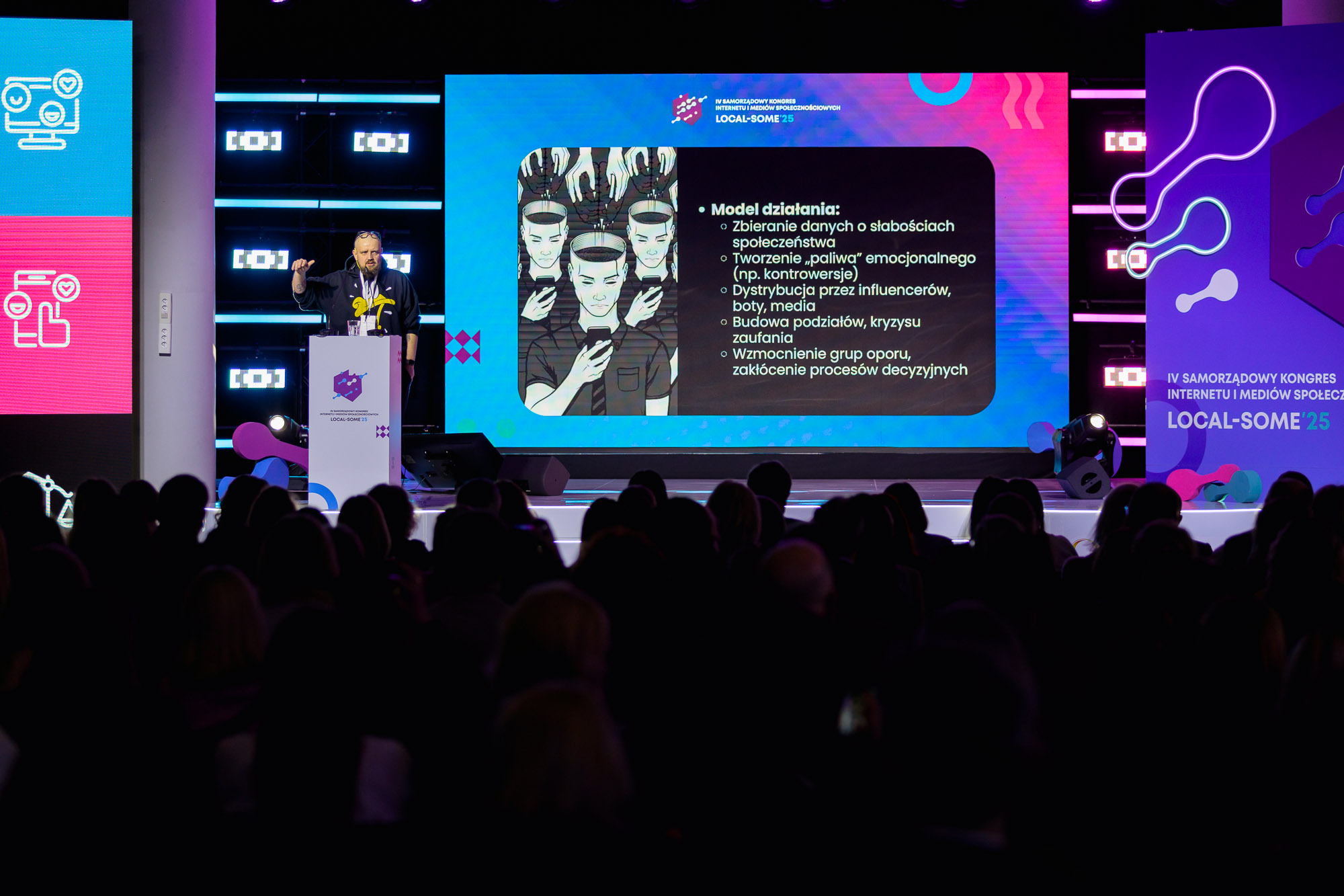 Sala konferencyjna, publiczność, scena, mężczyzna wyświetla prezentację na ekranie