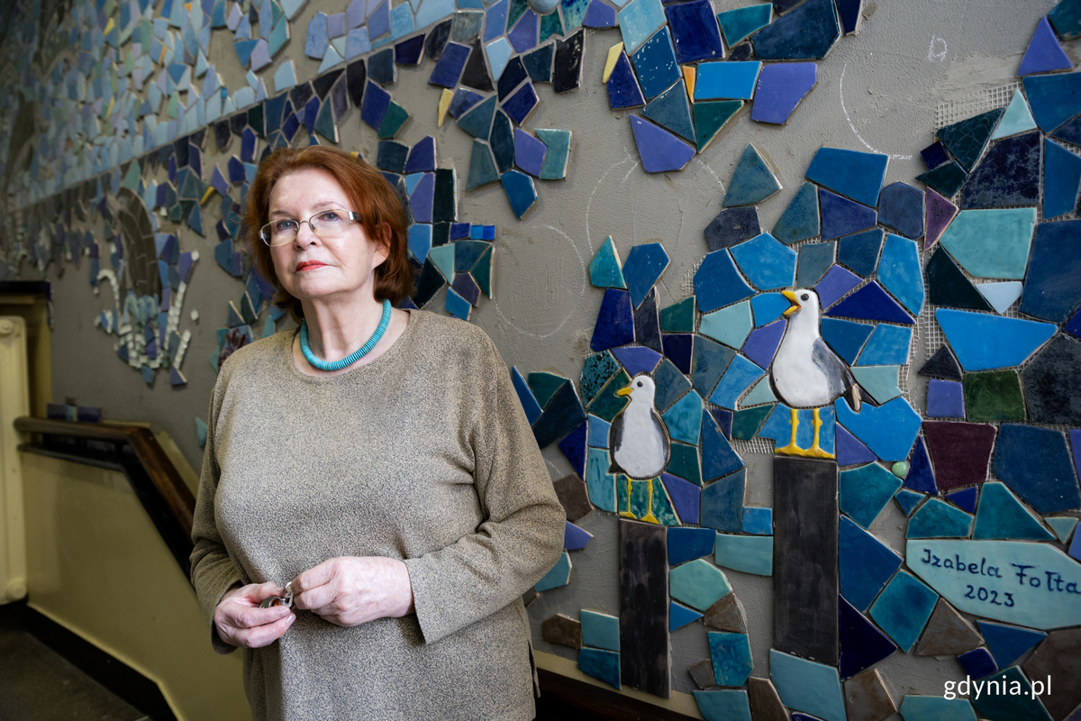 Kobieta stoi przy mozaice marynistycznej powstającej na ścianie.