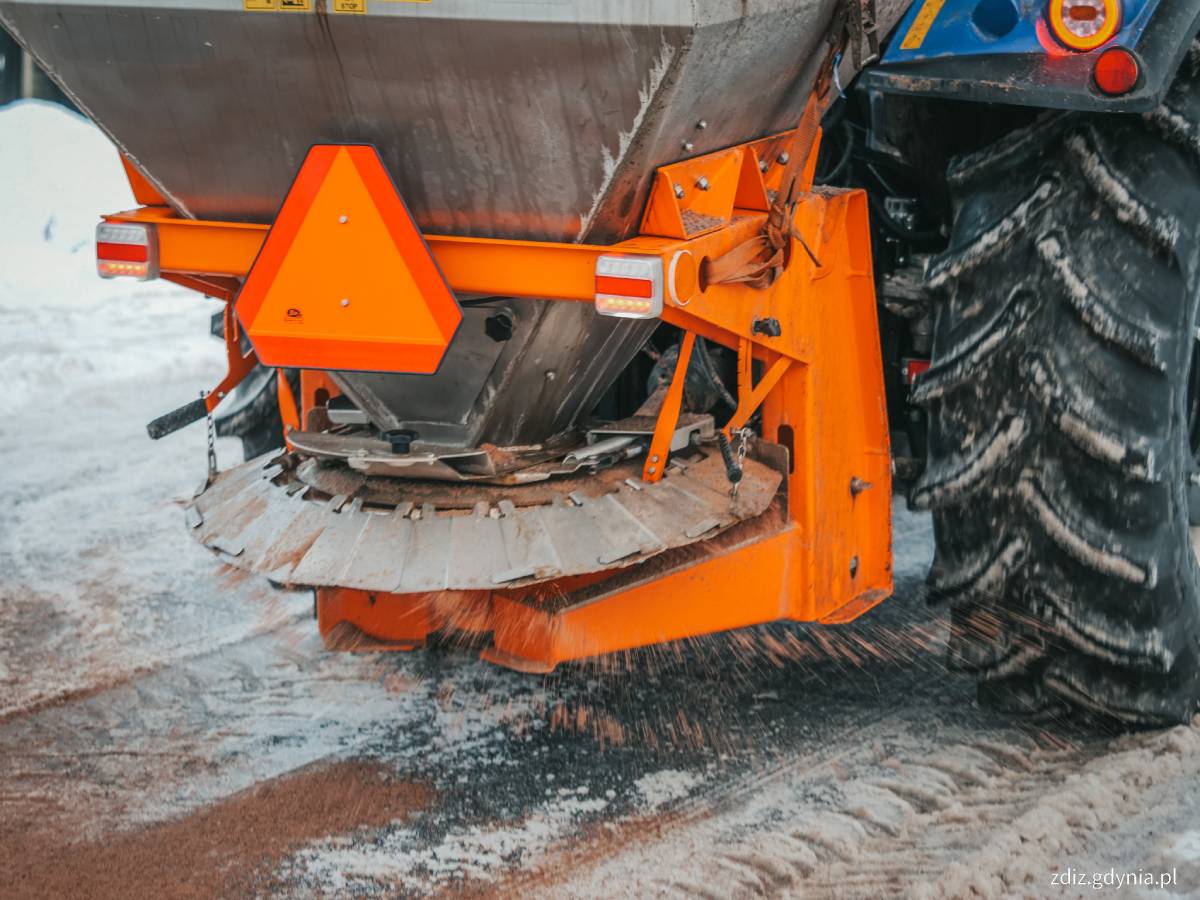 Zbliżenie na pomarańczowe urządzenie posypujące drogę solą zamontowane z tyłu traktora