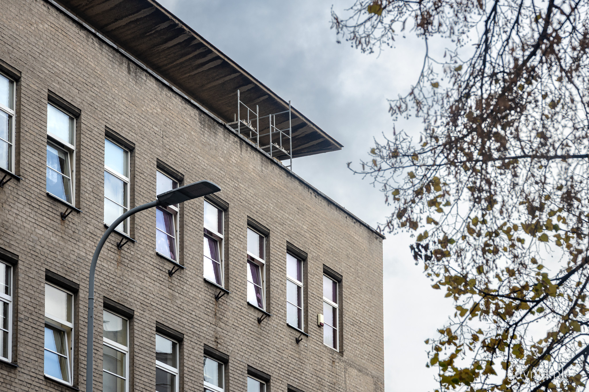 Budynek YMCA w Gdyni, fragment elewacji g&oacute;rnych pięter, widoczny gzyms na dachu i rusztowania, okna