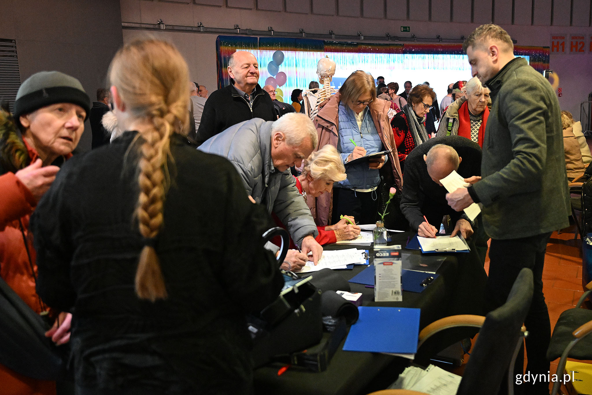 Wnętrze hali, grupa os&oacute;b, stolik z dokumentami