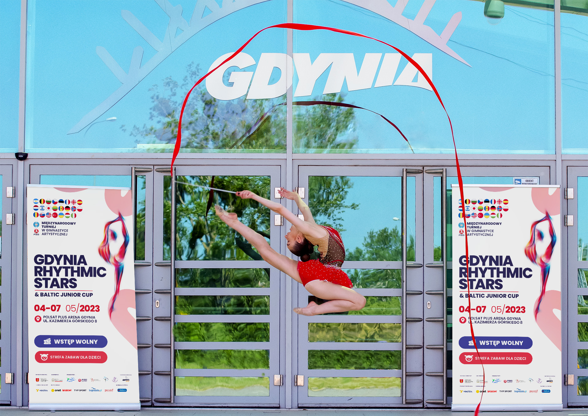 gimnastyczka z wstążką na tle wejścia do obiektu i dw&oacute;ch rollup&oacute;w