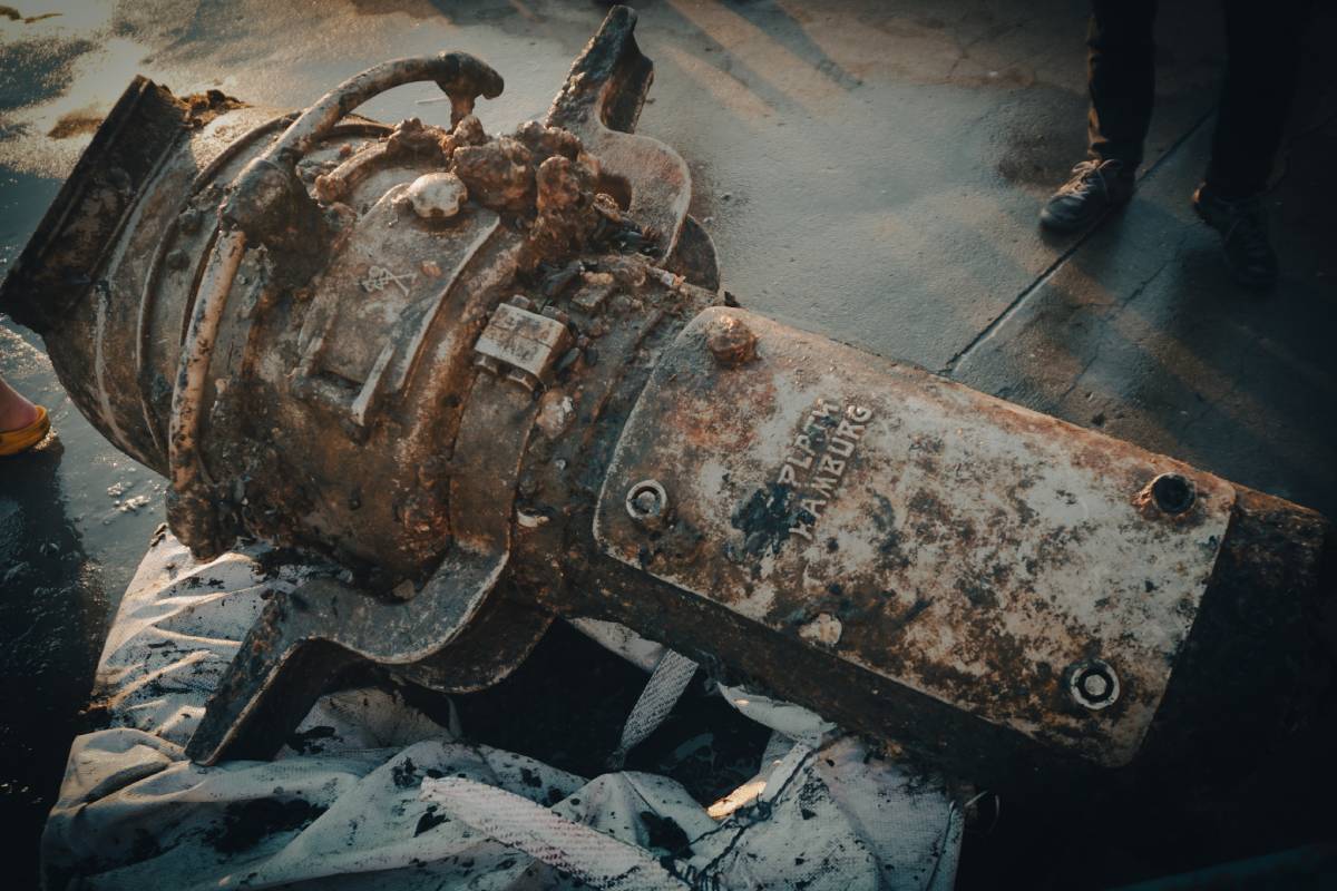 Brązowy metalowy element w kształcie walca leżący na drewnianym pokładzie statku