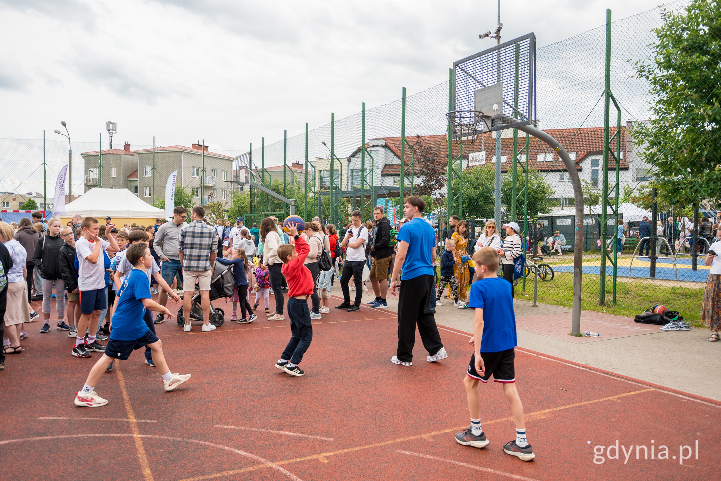 Boisko do koszyk&oacute;wki, tłum ludzi, kilkoro dzieci gra w koszyk&oacute;wkę