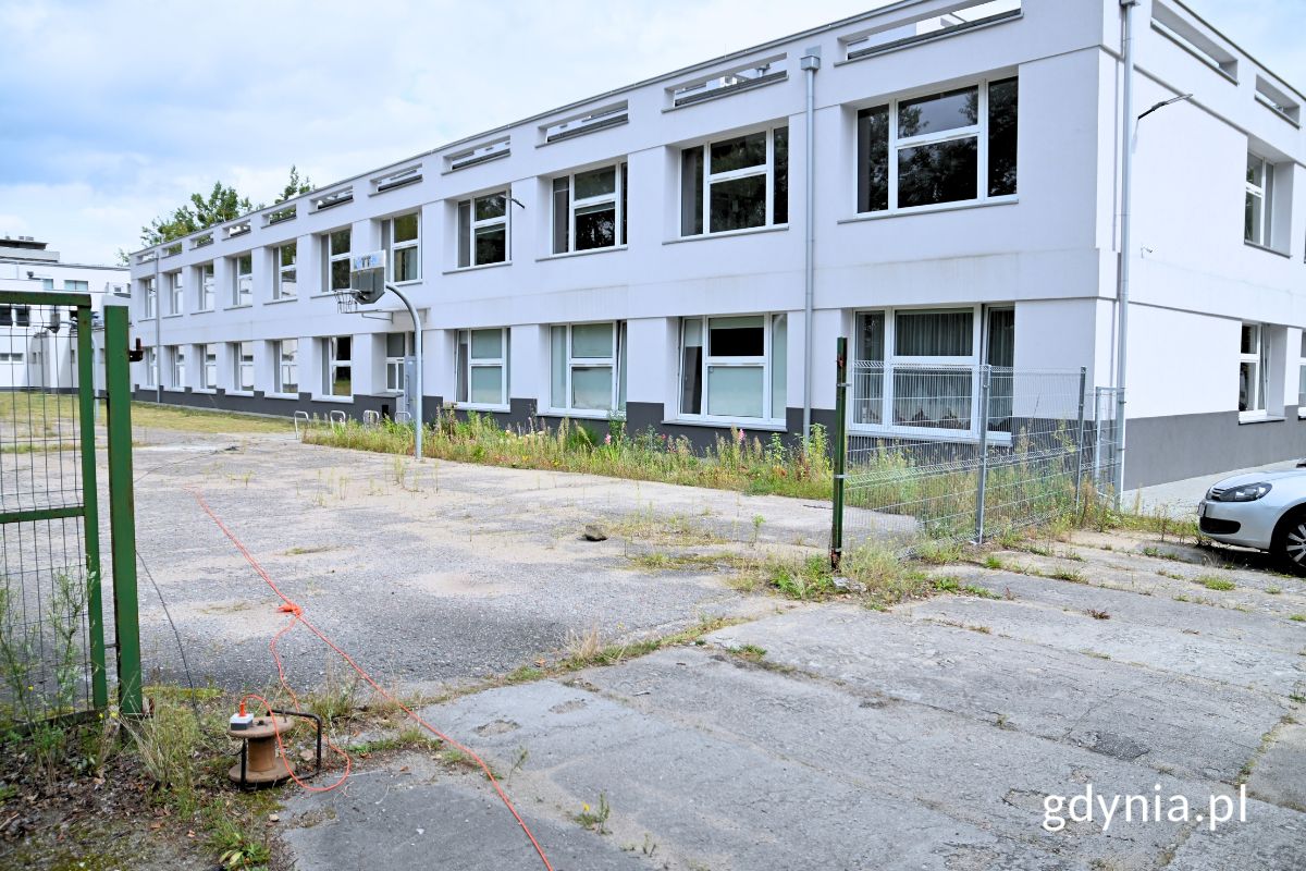 Budynek szkoły oraz fragment boiska i ogrodzenie oddzielające go od parkingu