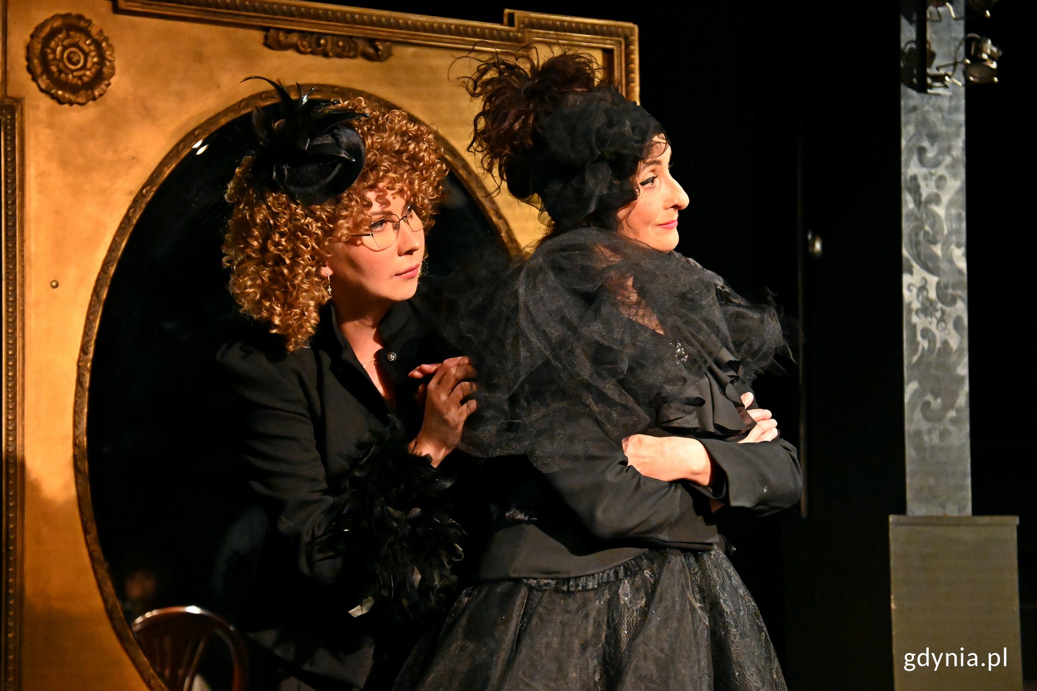 Zdjęcie z pr&oacute;by medialne spektaklu "Umrzeć ze śmiechu". Od lewej: Monika Babicka jako Millie oraz Elżbieta Mrozińska jako Lena stoją na tle owalnego lustra w dużej, grubej ramie // fot. Magdalena Czernek