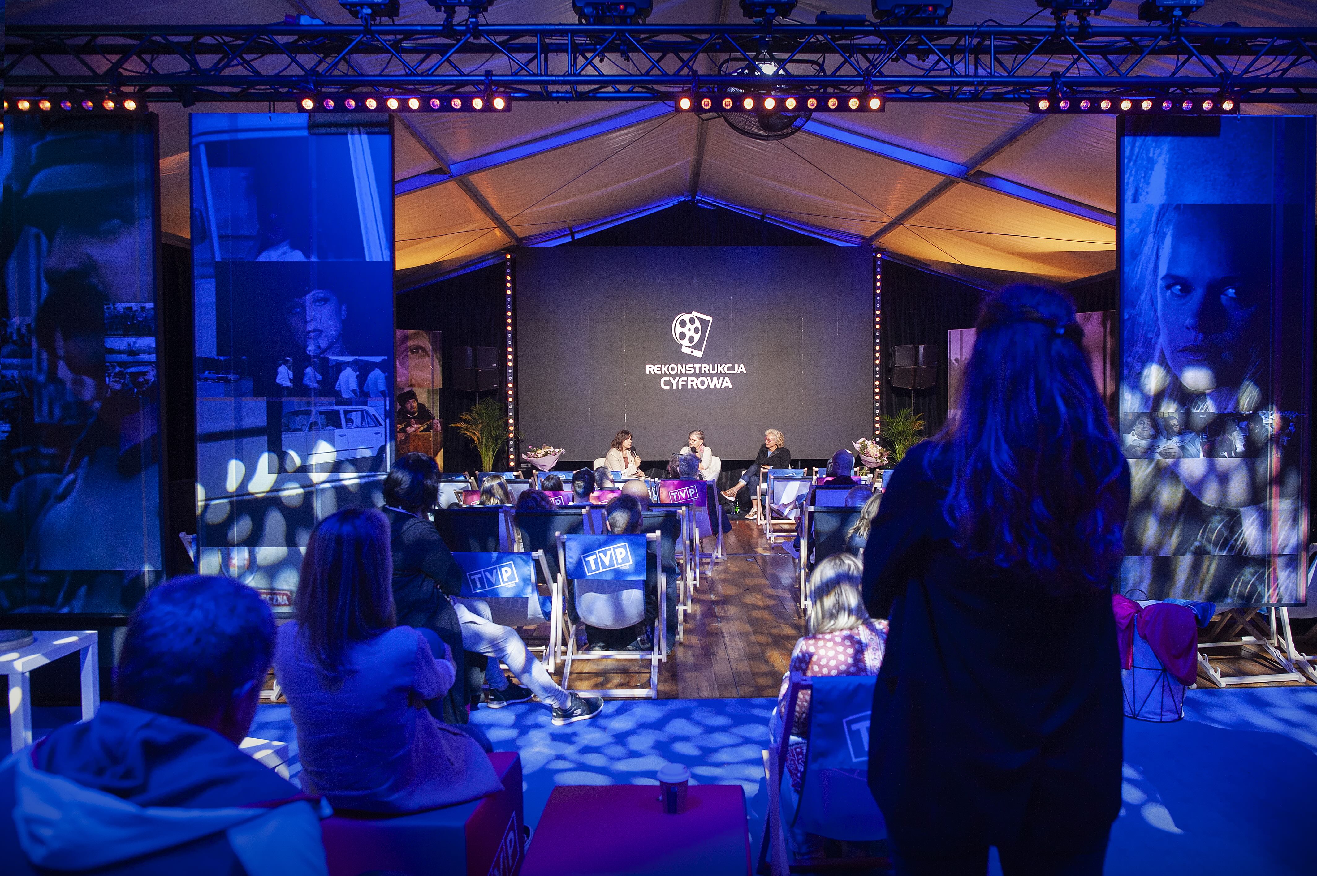 Scena na kt&oacute;rej przemawiają trzy kobiety. W tle plansza z napisem rekonstrukcja cyfrowa. Na pierwszym planie miejsca siedzące i publiczność