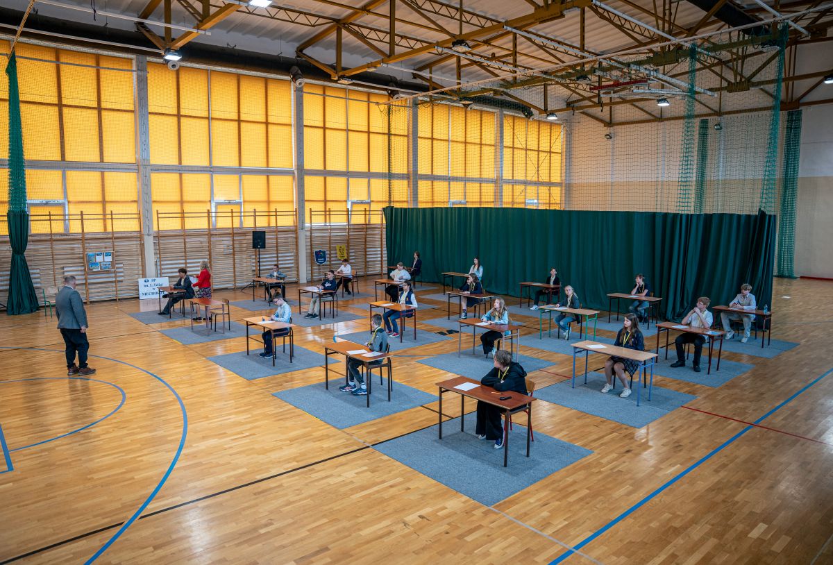 Uczestnicy konkursy wiedzy o Morzu podczas zmagań przy biurkach na sali gimnastycznej.