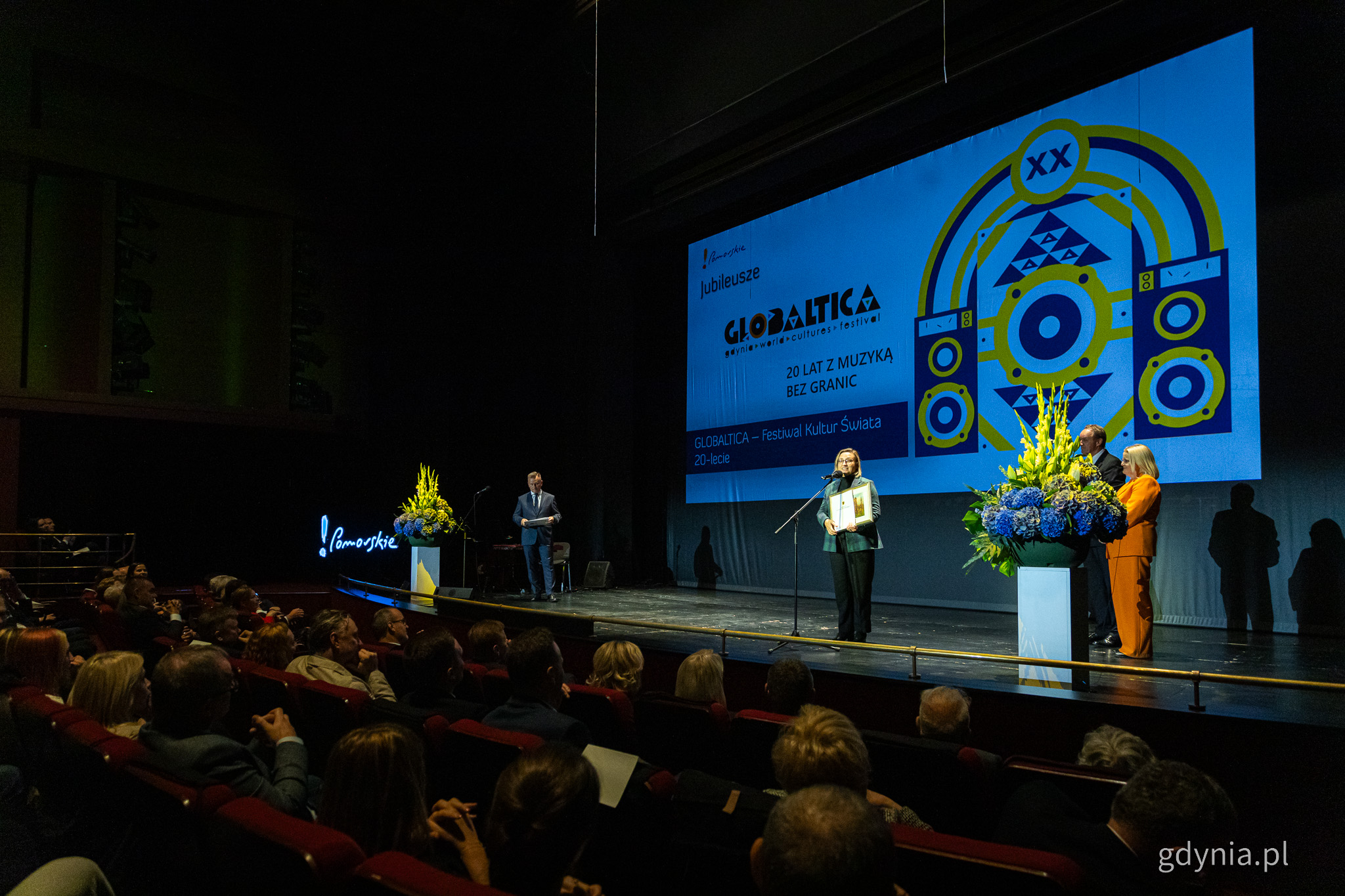 Scena, na ekranie logotyp Globaltica, kilka os&oacute;b na scenie, kobieta przemawia przez mikrofon