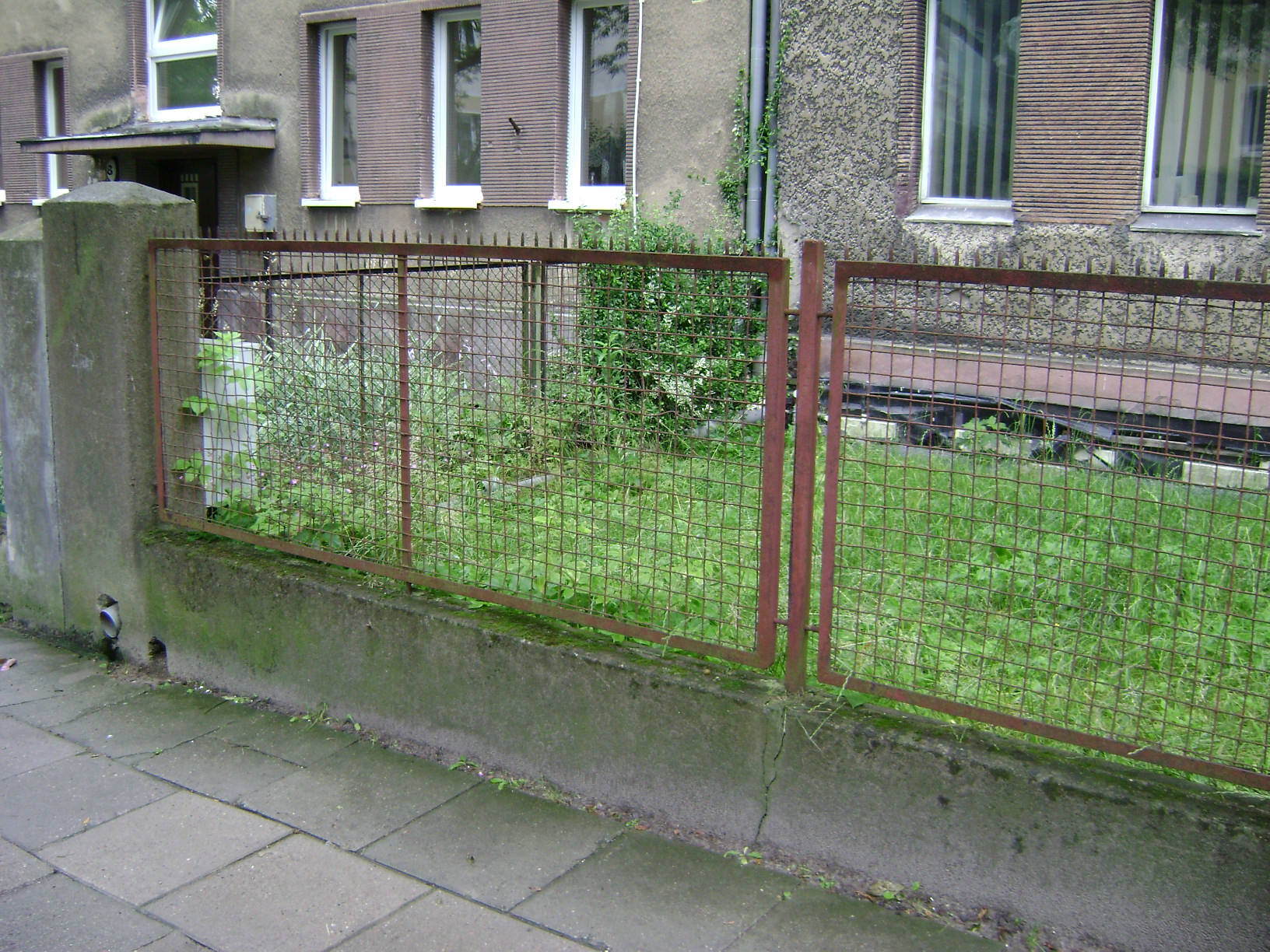 Ogrodzenie z metalowej siatki w ramach mocowanych do murowanych słupk&oacute;w, charakterystyczne dla lat 30. XX w. 