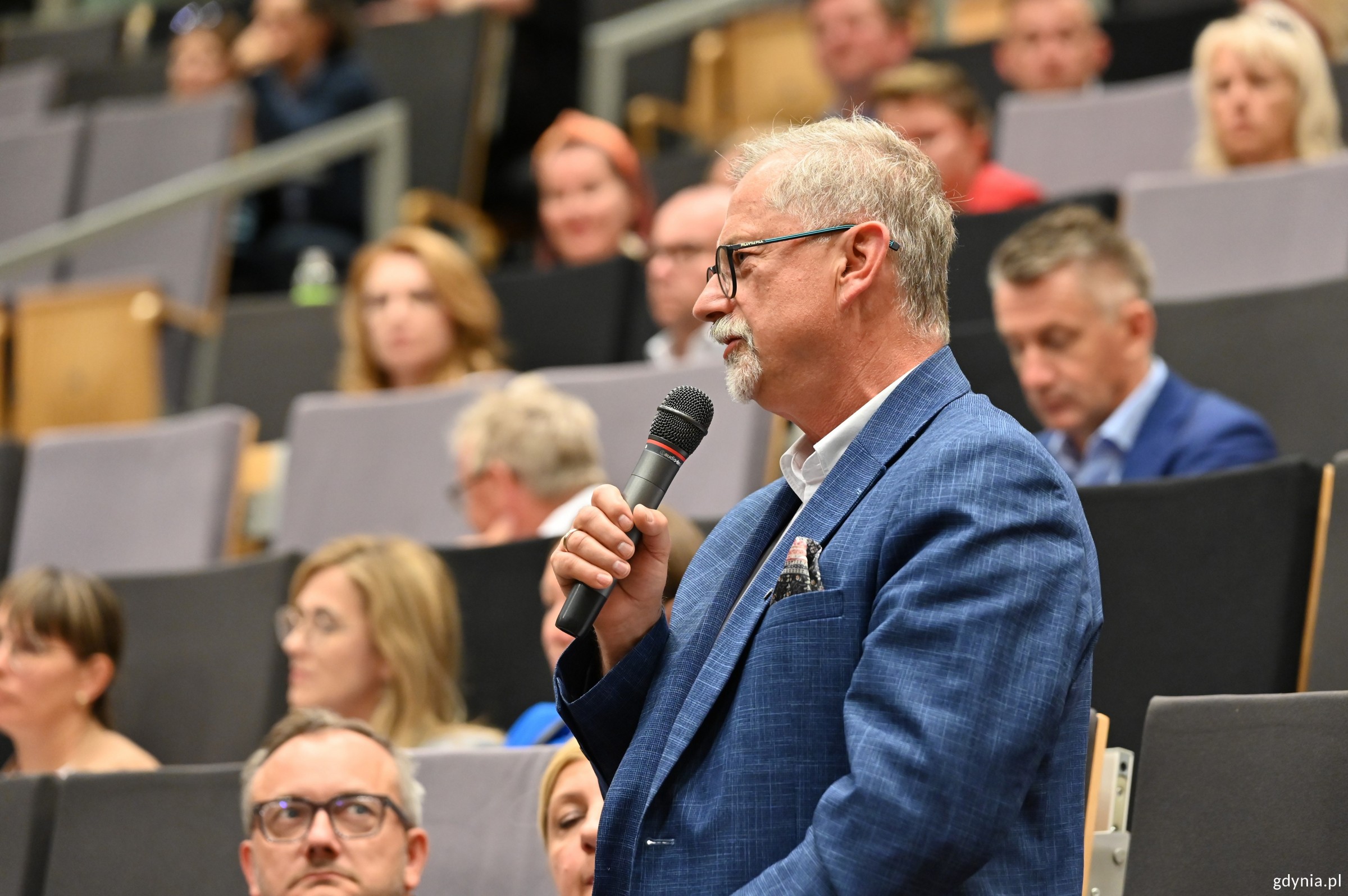 Mieszkaniec zadający pytanie do mikrofonu na auli pełnej ludzi