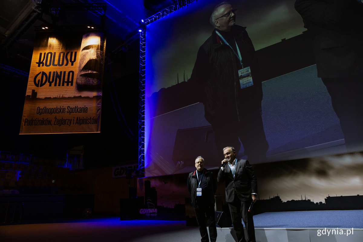 Dw&oacute;ch mężczyzn z mikrofonami na hali podczas wydarzenia.