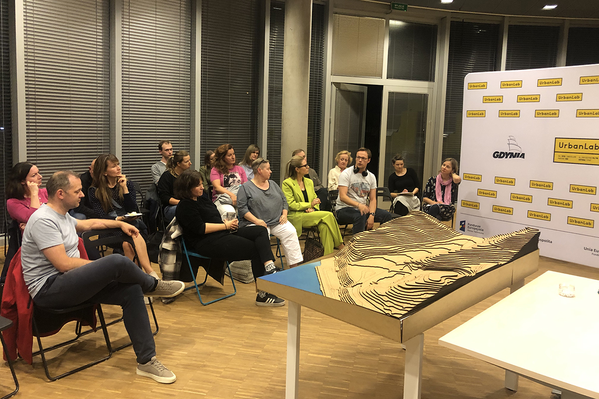 Grupa os&oacute;b siedzi i rozmawia w sali.