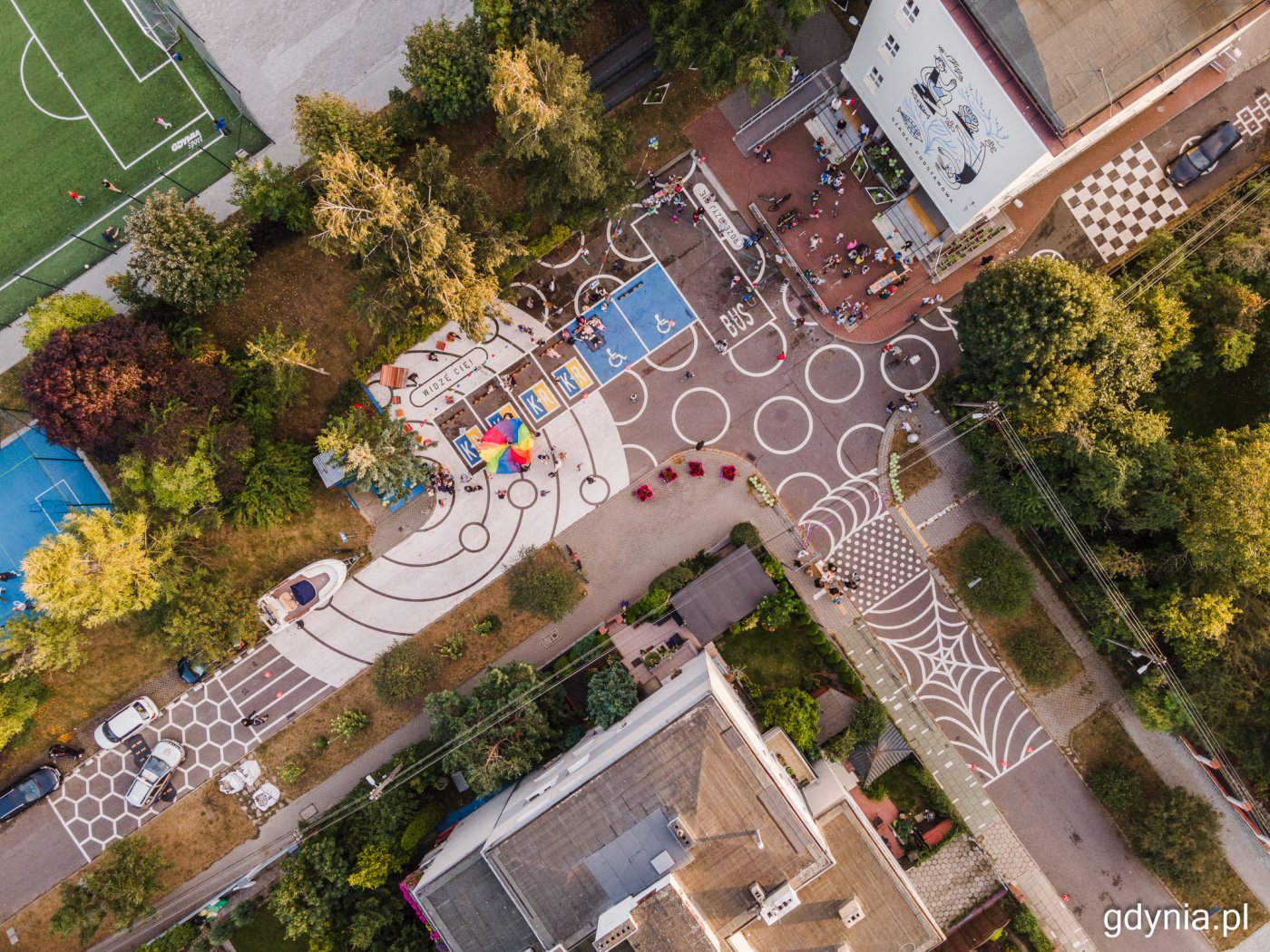 Zdjęcie z drona, mural namalowany na szkolnym parkingu, tłum dzieci i dorosłych, obok budynek