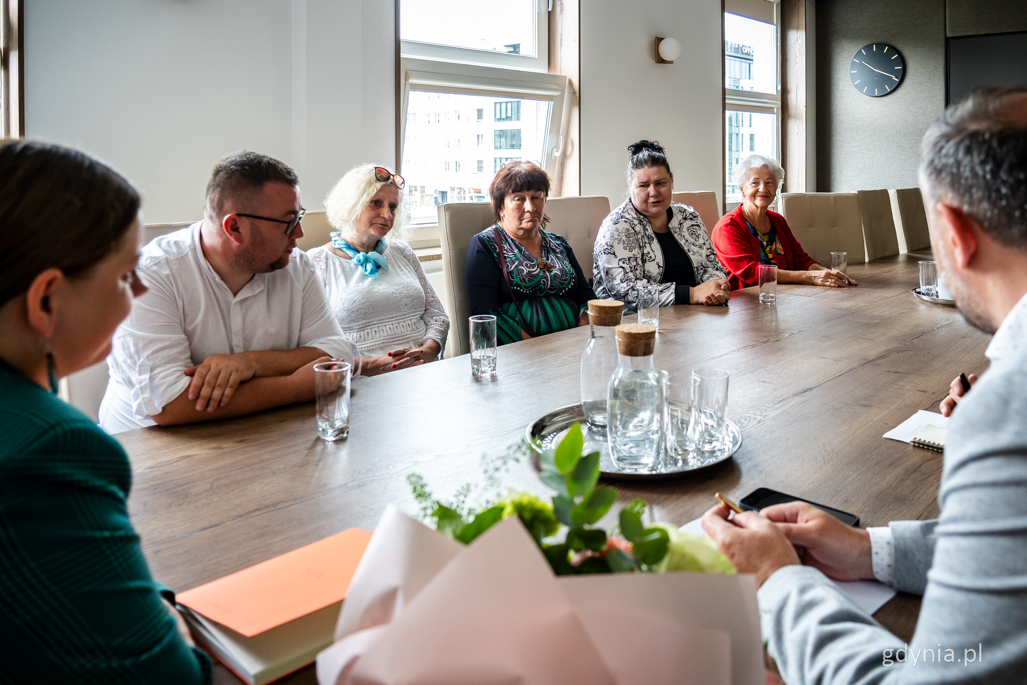 Sala w Urzędzie Miasta Gdyni, przy stole siedzi kilka os&oacute;b z Gdyńskiej Rady Rodzinnej Pieczy Zastępczej. W tle okna, po bokach widoczna prezydent Aleksandra Kosiorek i dyrektor Tomasz Augustyniak