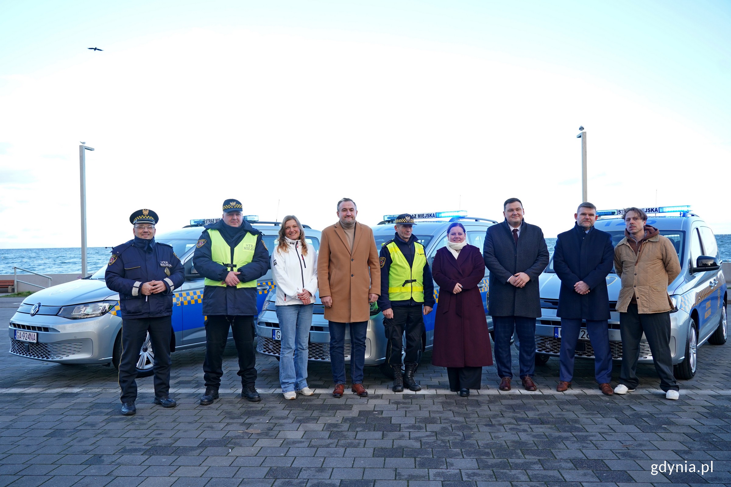 Od prawej: radny miasta Łukasz Piesiewicz, Robert Ronduda &ndash; naczelnik Wydziału Zarządzania Kryzysowego i Ochrony Ludności, Łukasz Kobus &ndash; sekretarz miasta i dyrektor generalny Urzędu Miasta Gdyni, prezydent Aleksandra Kosiorek, wiceprezydent Tomasz Augustyniak, radna miasta Natalia Kłopotek-Gł&oacute;wczewska i Andrzej Bień &ndash; komendant Straży Miejskiej w Gdyni ze strażnikami przy nowych radiowozach Straży Miejskiej w Gdyni (fot. Magdalena Czernek)