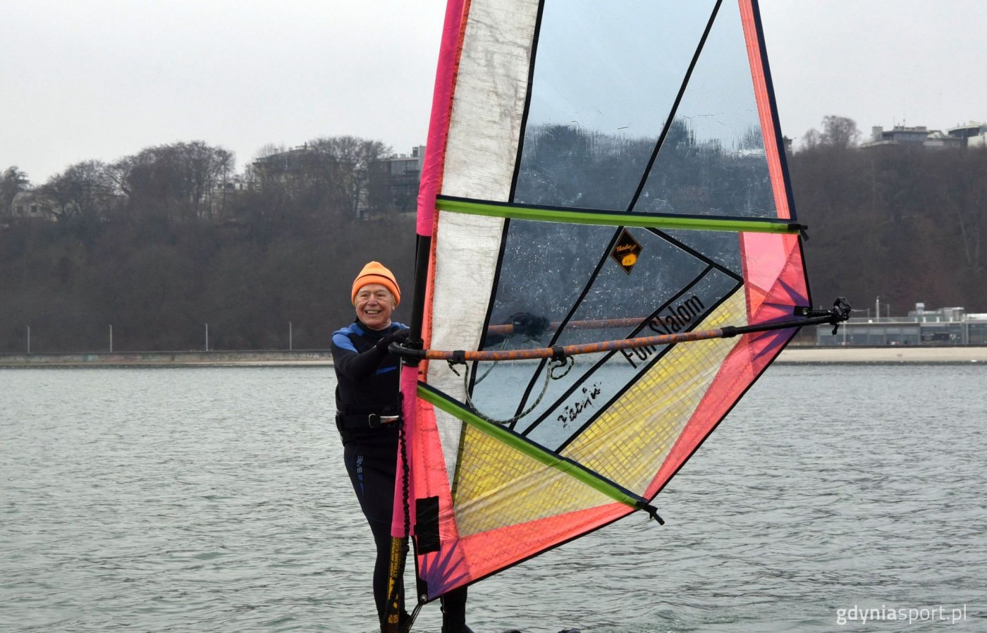 Piotr Dudek płynie na desce surfingowej, w tle plaża Gdynia Śr&oacute;dmieście / fot. M. Urbaniak