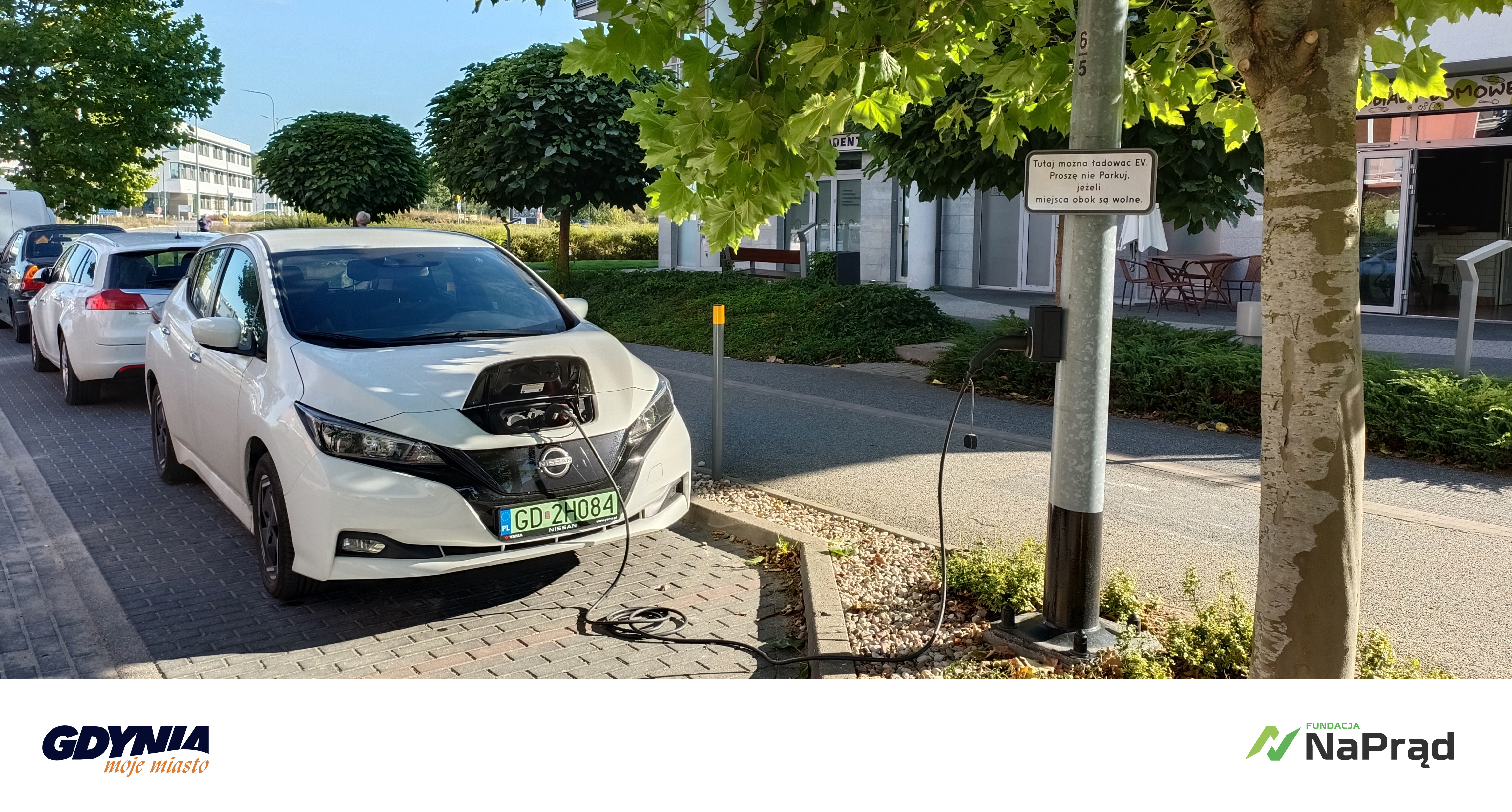 &bdquo;Electric Street&rdquo; - wsp&oacute;lny projekt miasta Gdynia i Fundacji #NaPrąd. Zdjęcie samochodu elektrycznego w zatoczce, podłączony kablem do słupa oświetleniowego. Obok inne samochody, ulica, budynki