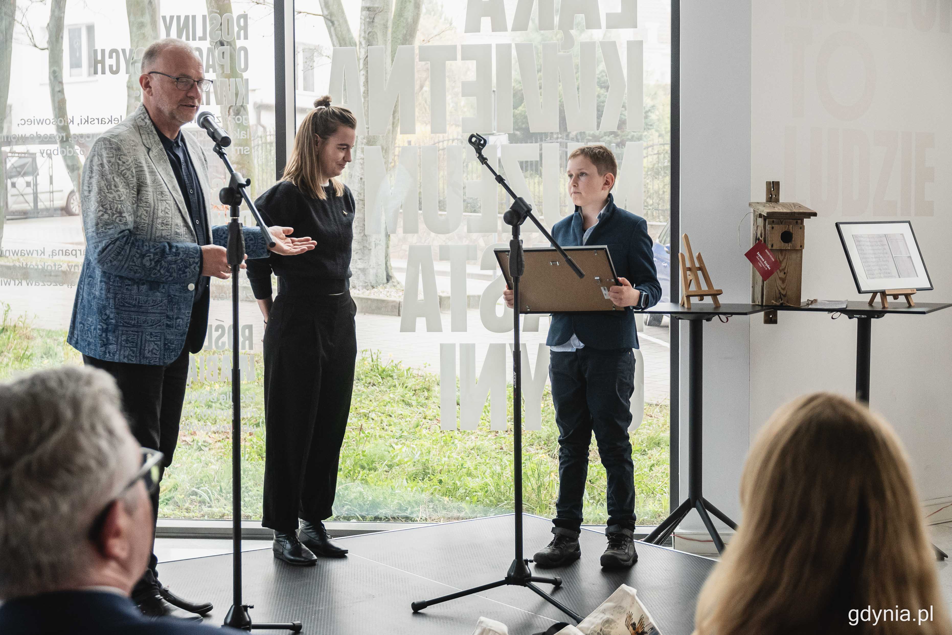 Szymon Usydus (z prawej) odbiera nagrodę - SuperBudkę - za swoją konkursową pracę od Michała Gucia (z lewej) i Zofii R&oacute;życkiej (w środku), fot. Kamil Złoch