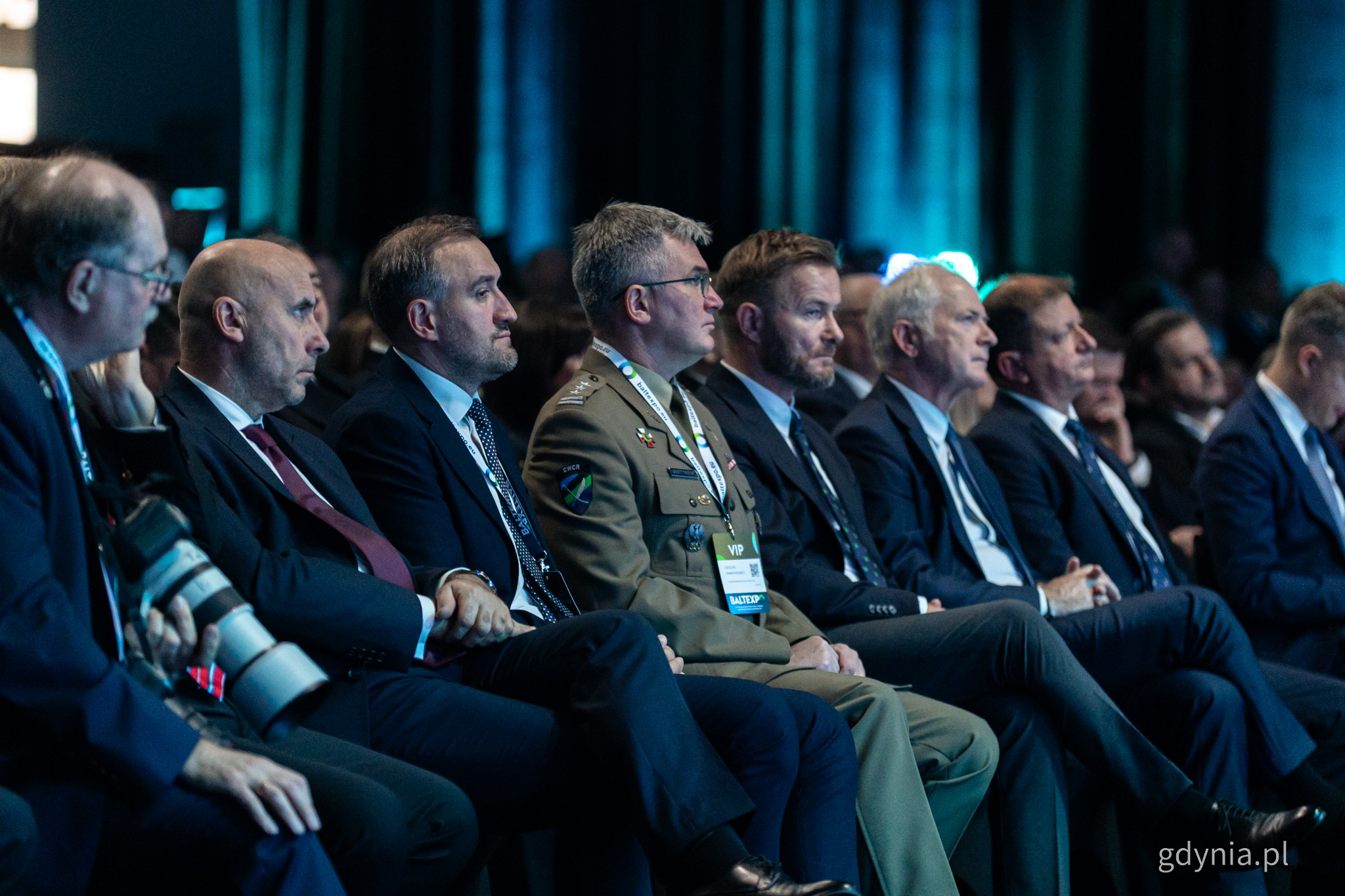 Sala konferencyjna AmberExpo, ciemne tło, pierwszy rząd, wszystkie miejsca zajęte, siedzi m.in. Tomasz Augustyniak