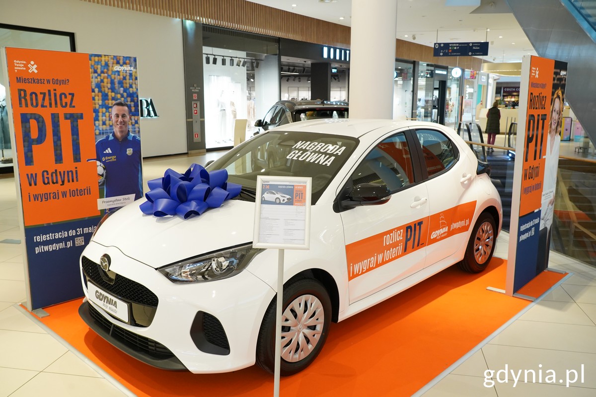 Hol w Centrum Riviera, na pomarańczowym dywanie stoi biała Mazda 2, obok logotypy i ekspozycja Rozlicz PIT w Gdyni
