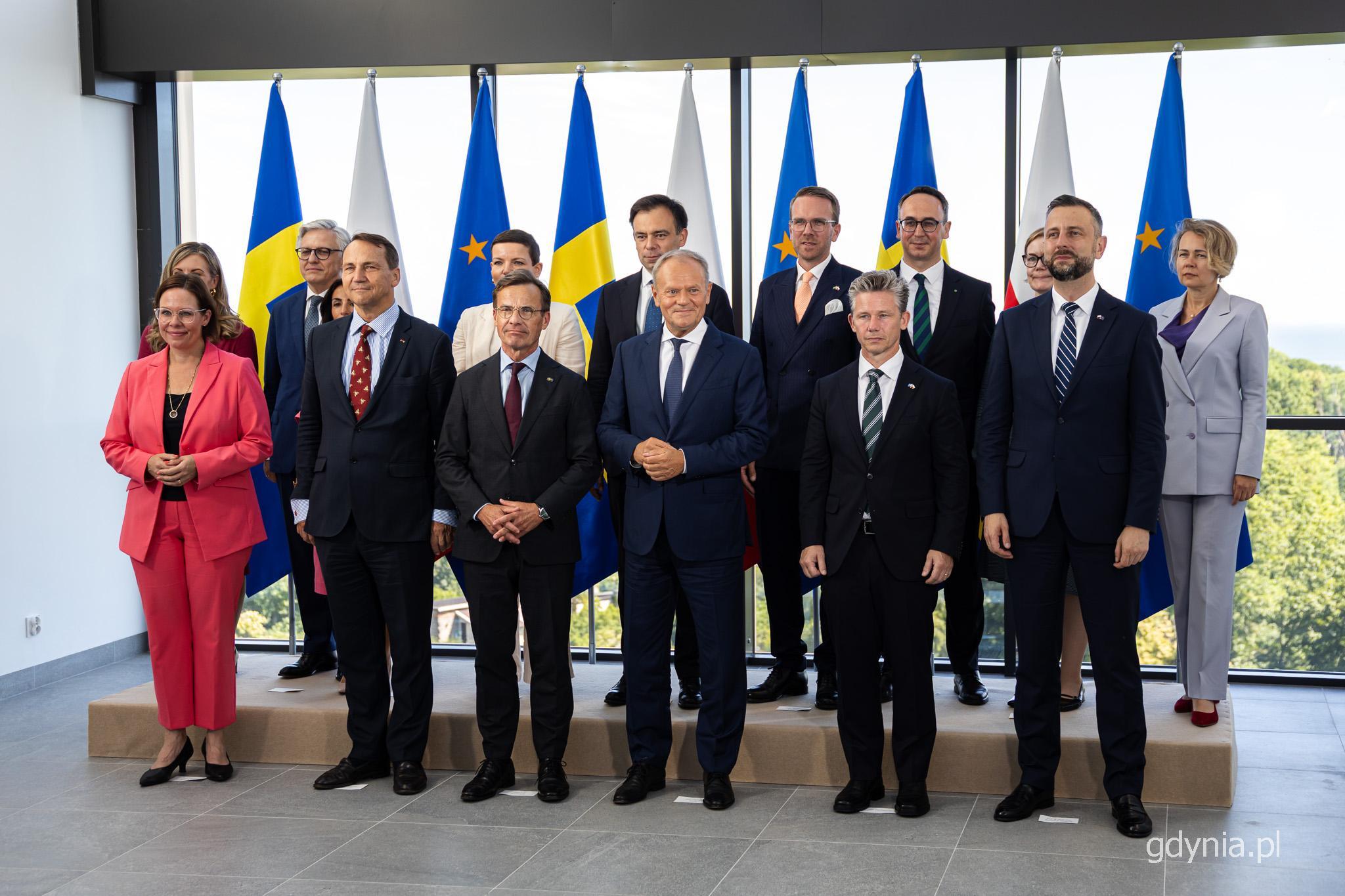 Pomieszczenie w Akademii Marynarki Wojennej w Gdyni, do zdjęcia na tle flag narodowych pozuje grupa przedstawicieli rządu Polski i Szwecji, w tym premierzy obu państw