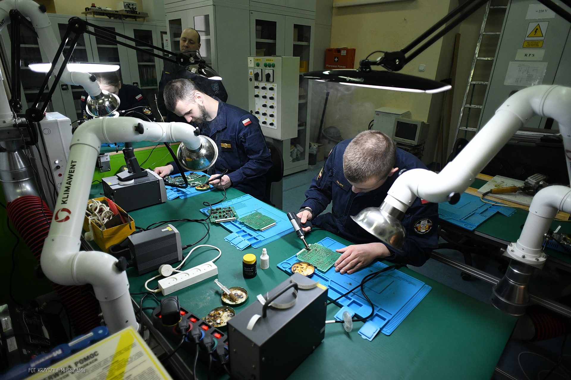 Pracownia AMW, studenci w granatowych uniformach przy stole, na stole układy scalone, aparatura