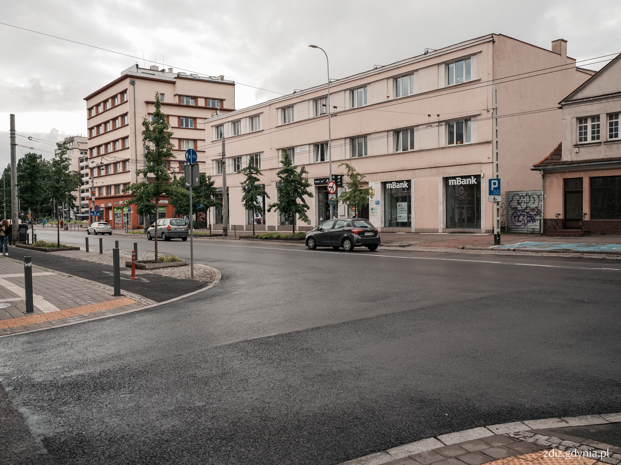 skrzyżowanie z nową nawierzchnią, widoczny asfalt, w tle budynki i ruch uliczny